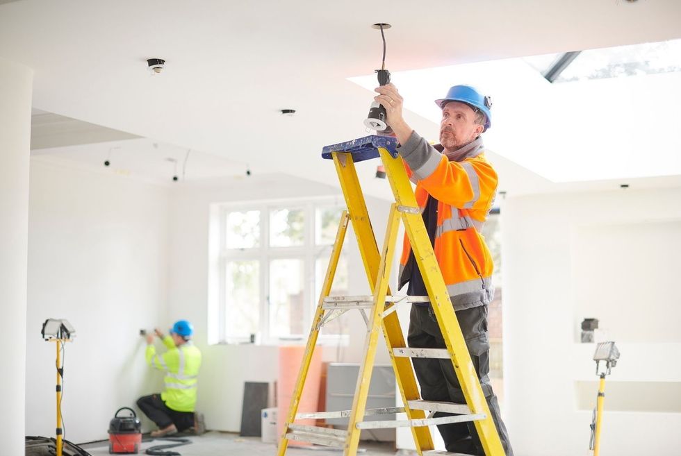 A man is standing on a ladder working on a ceiling.