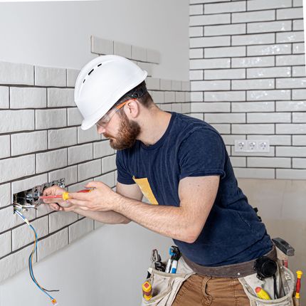 A man wearing a hard hat and safety glasses is working on a brick wall.