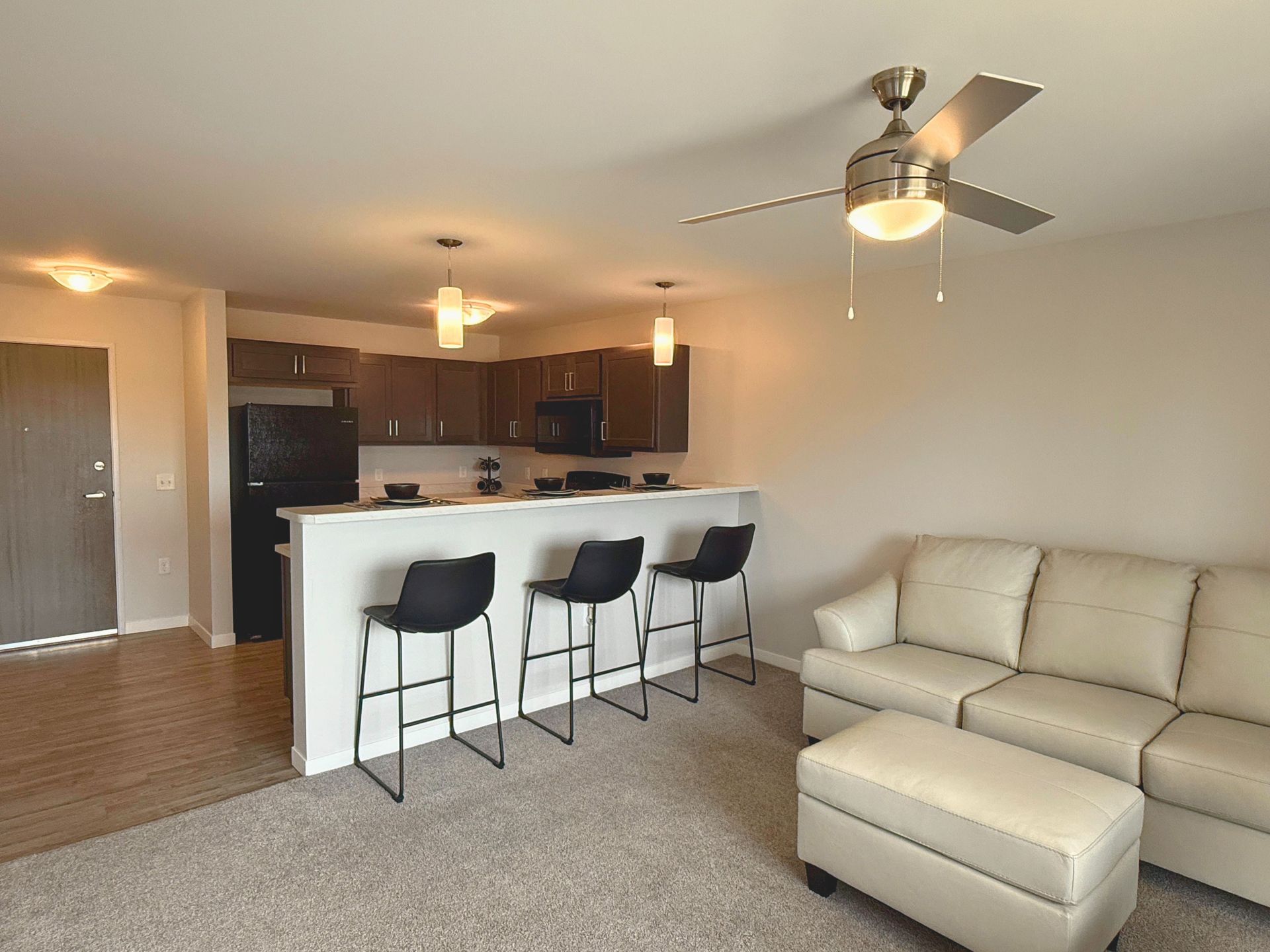 Modern apartment living room with beige sectional, bar stools, and open kitchen with dark cabinets