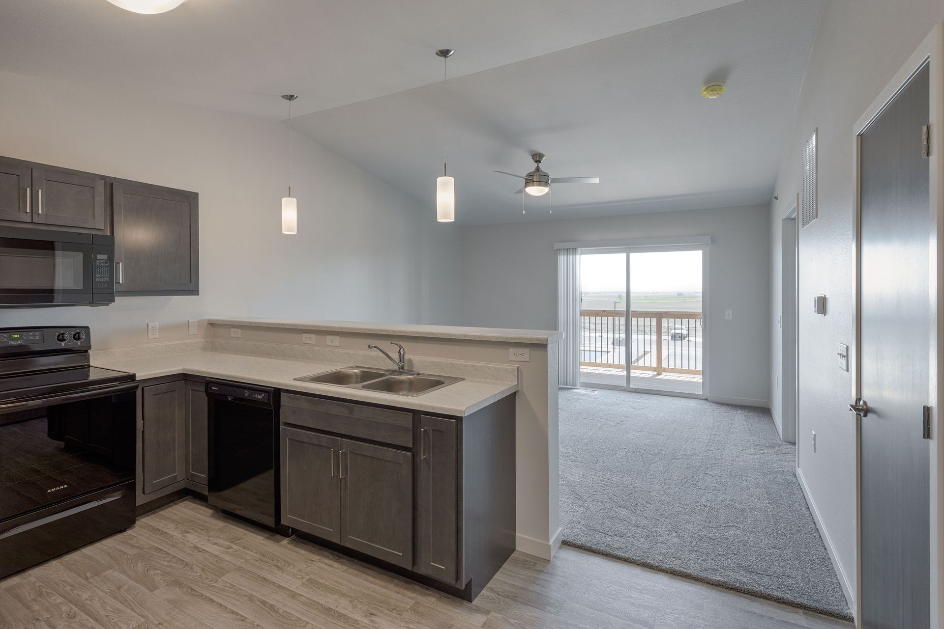 Modern kitchen with dark cabinets, granite island, and an open view to a bright living area and balcony.