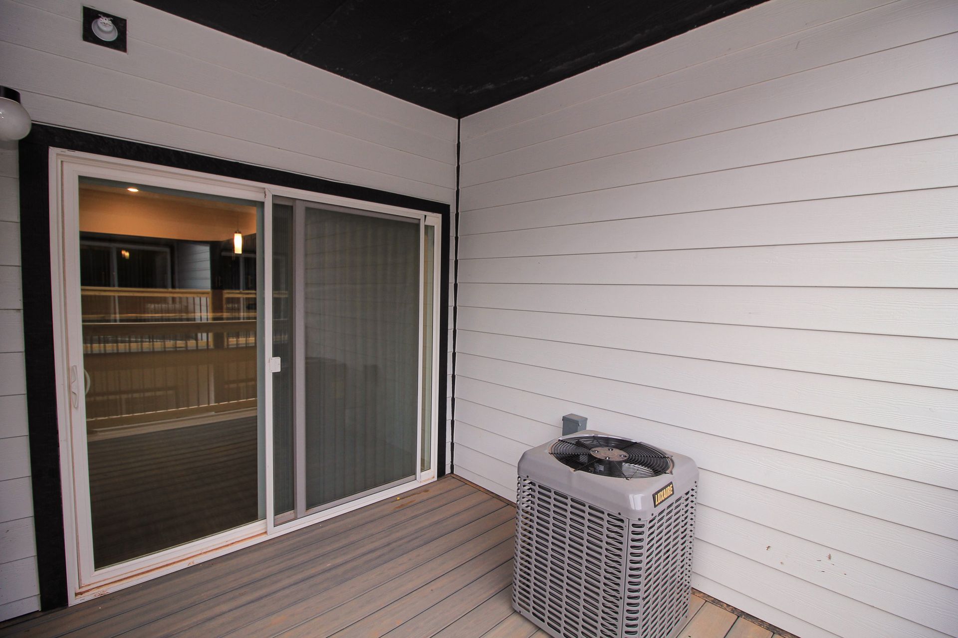 Empty covered balcony with gray deck boards, white siding, and a small AC unit.