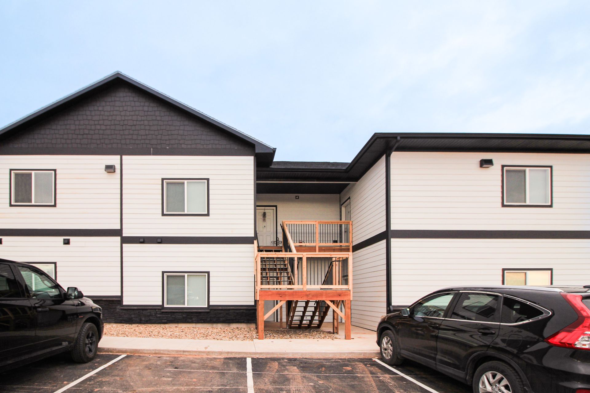 Apartment building with central stairway and parked cars in front under a cloudy sky