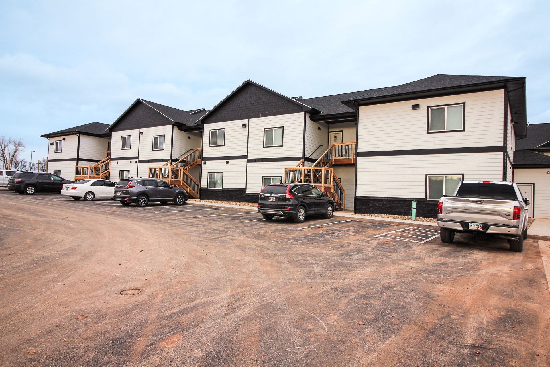 Apartment building with parked cars on a dirt lot, viewed from the front