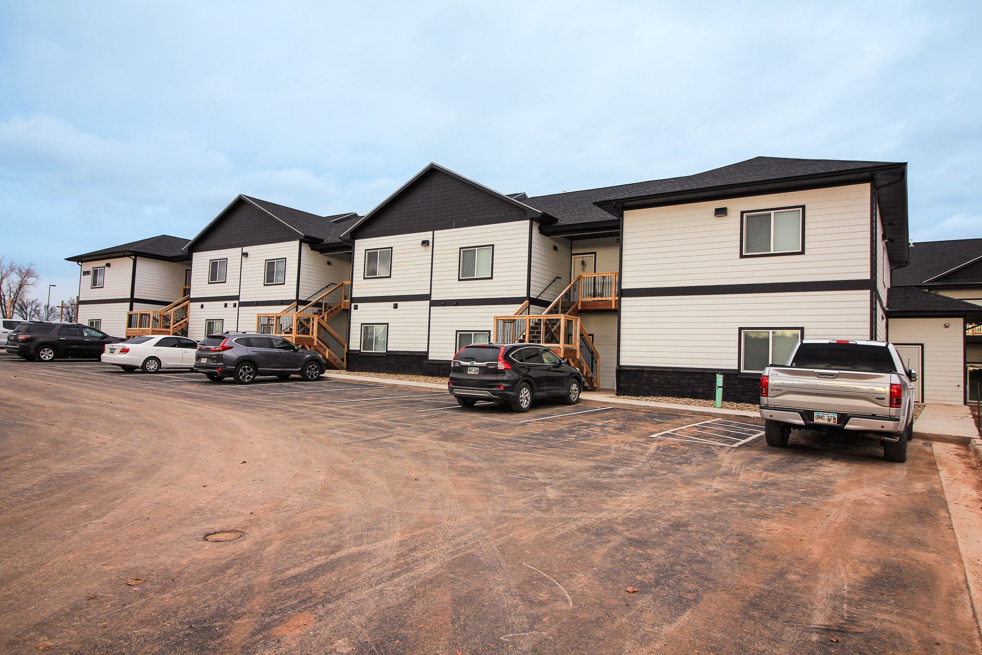 Row of modern townhouses with parked cars on a gravel lot under a cloudy sky