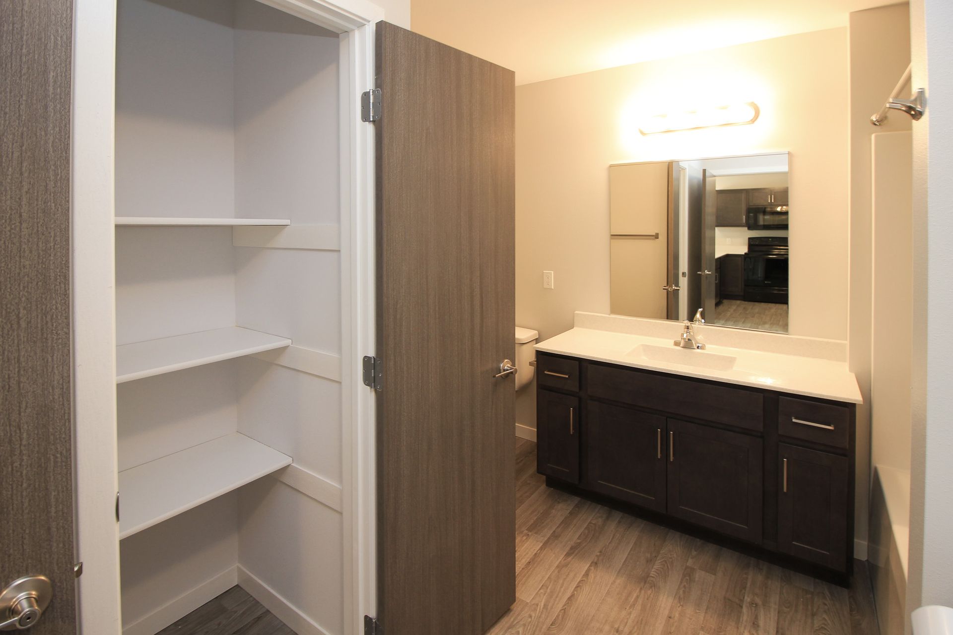 Bathroom with open white shelves, dark vanity, large mirror, and warm lighting