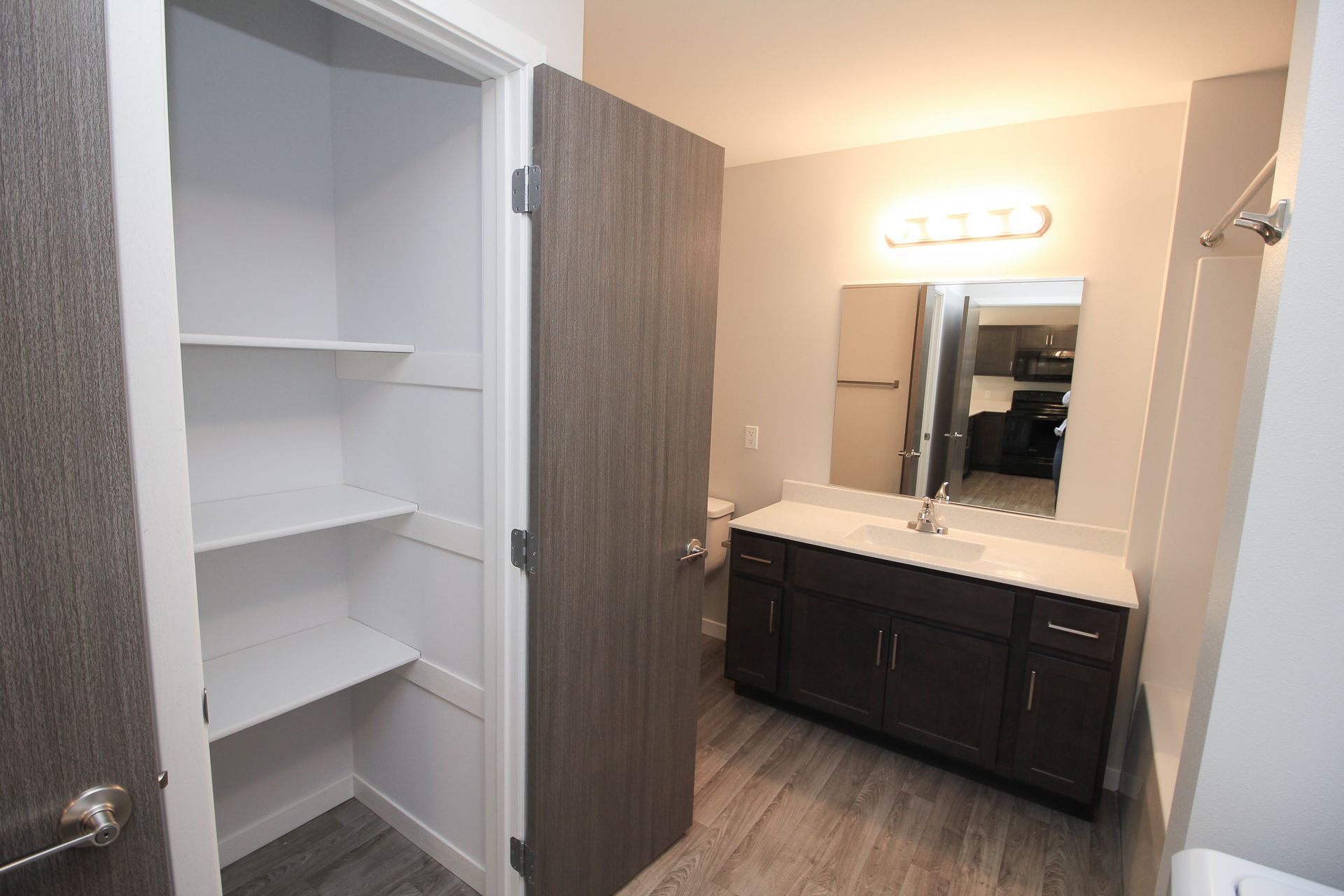 Bathroom vanity with mirror, dark cabinets, and an open white shelving closet in a modern interior.