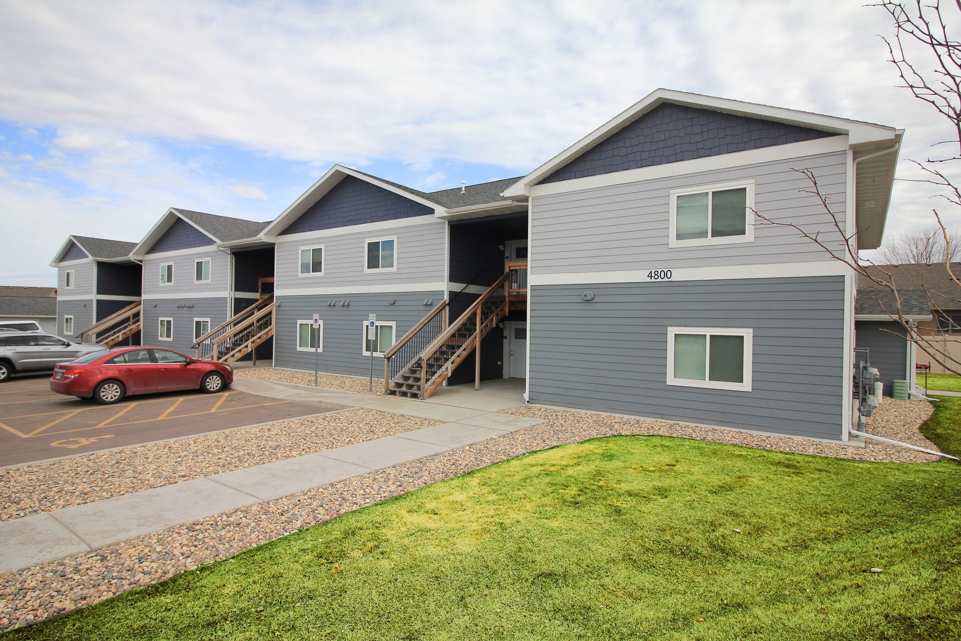 Apartment buildings with gray siding, a red car, and a grassy courtyard in front
