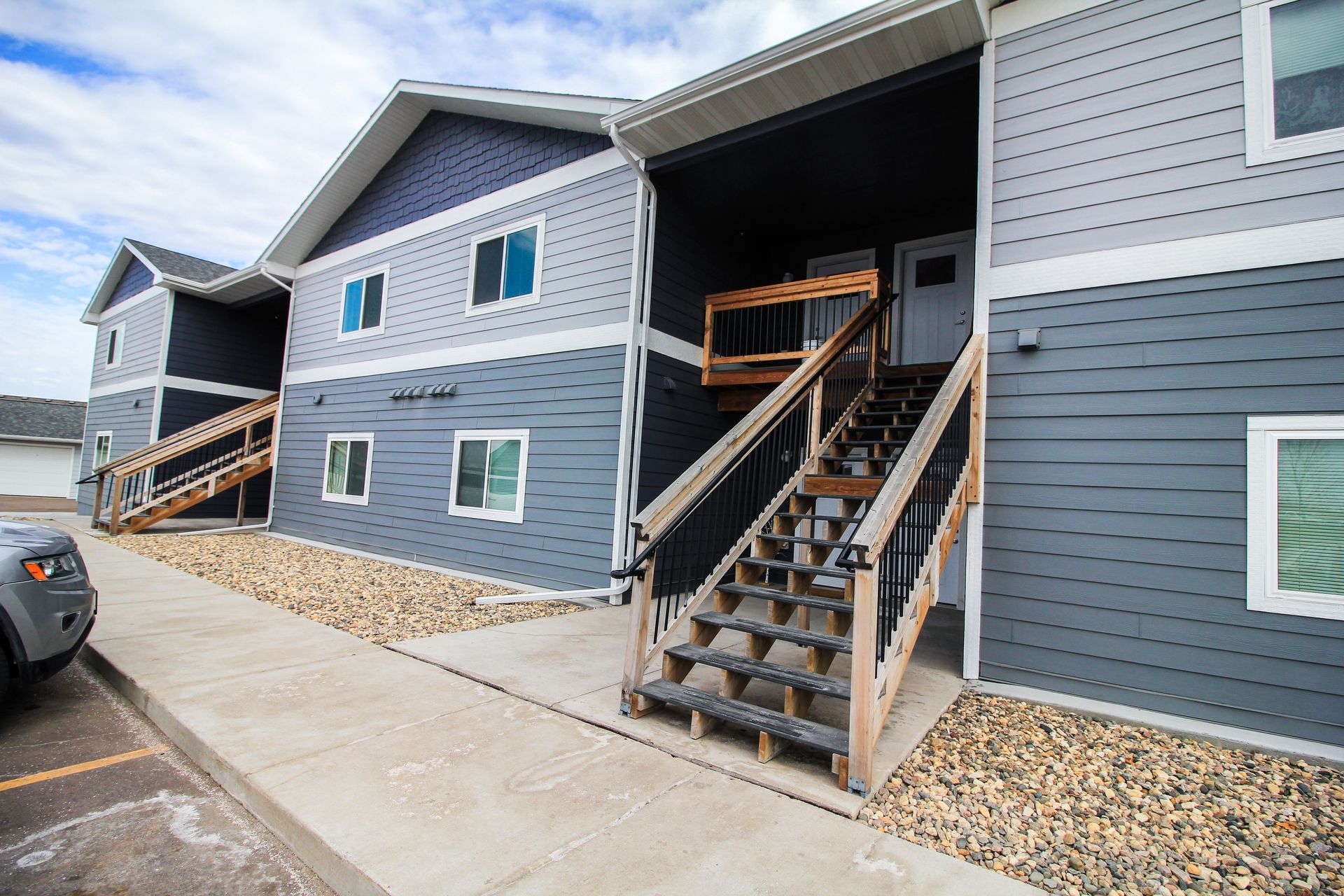 Apartment building entrance with exterior stairs and blue-gray siding on a concrete walkway