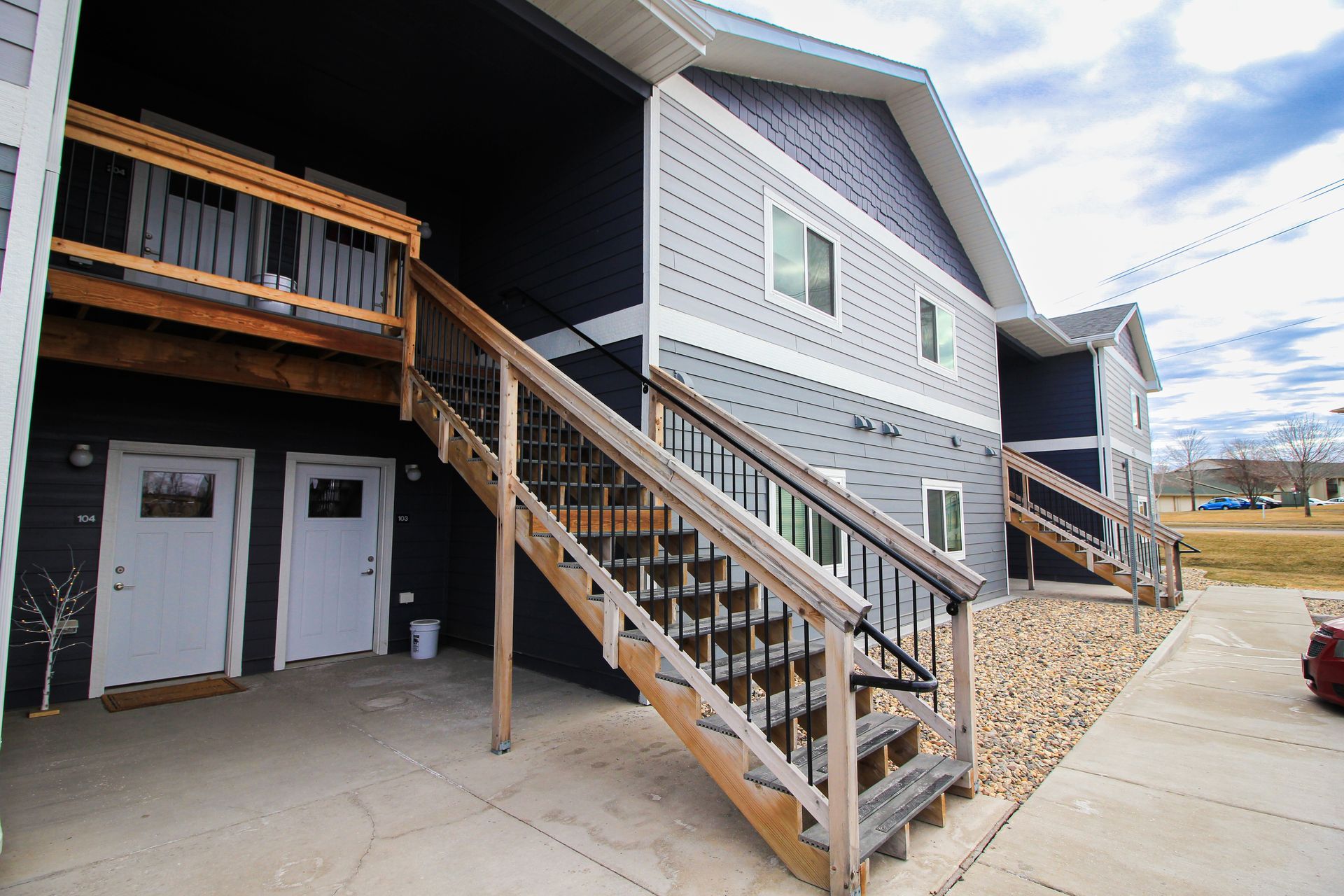 Exterior of a duplex with an outdoor staircase, covered porch, and garage-style doors under a balcony