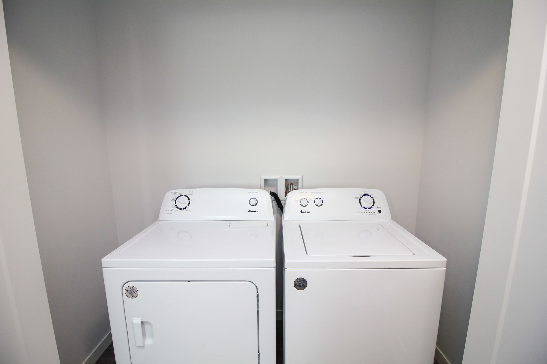 Two white laundry machines side by side in a small alcove with gray walls
