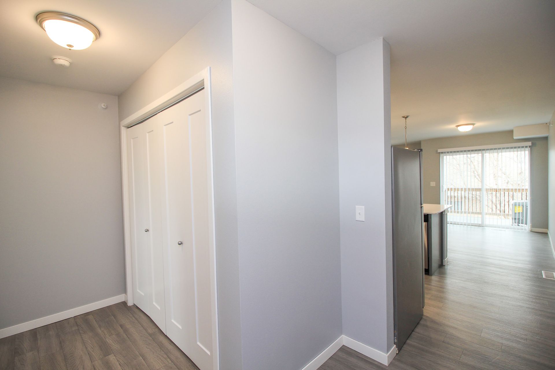 Bright apartment hallway with white closet doors, gray walls, and a view into a kitchen and living area.