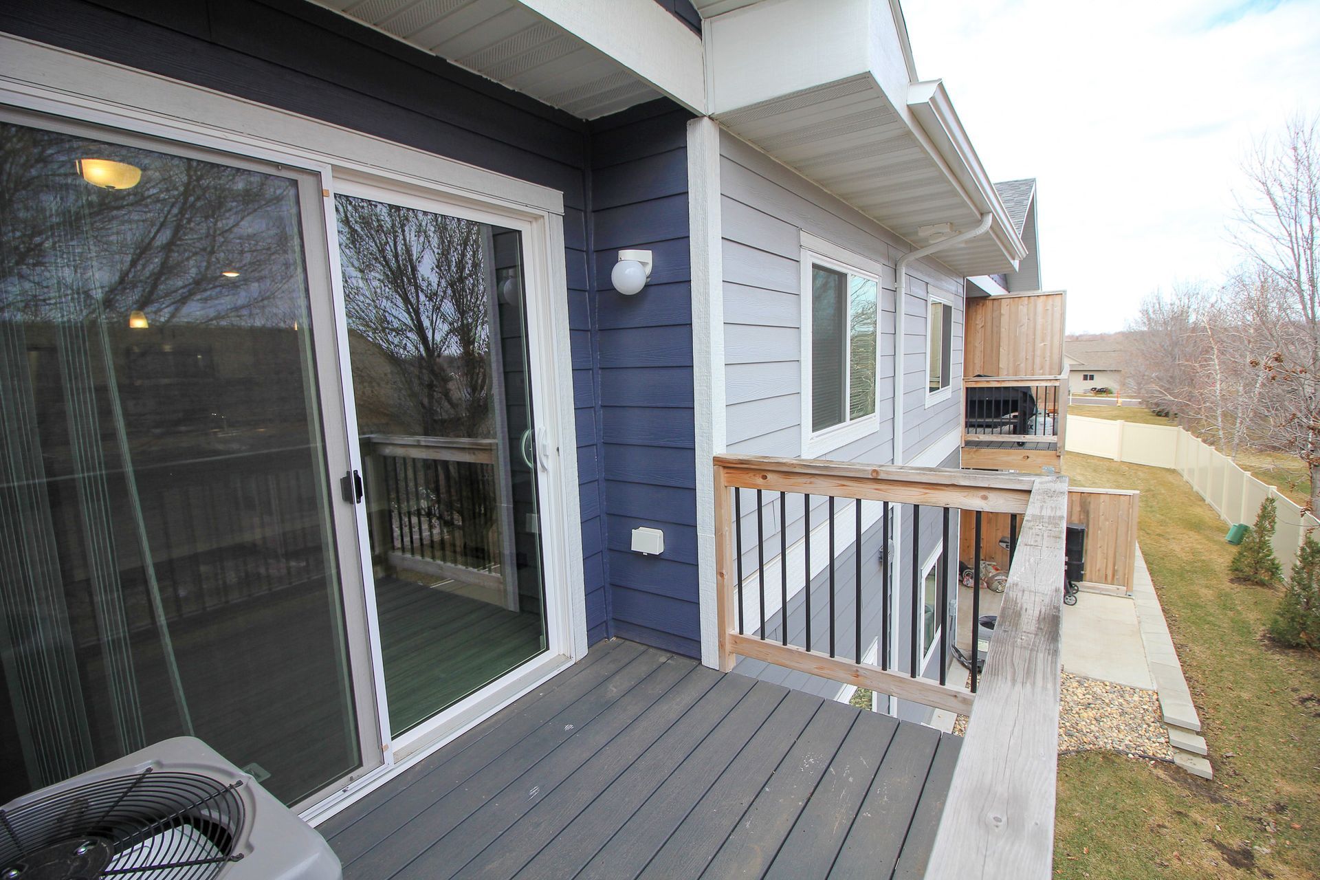 Back deck with sliding glass door, blue siding, white railing, and a narrow yard beyond