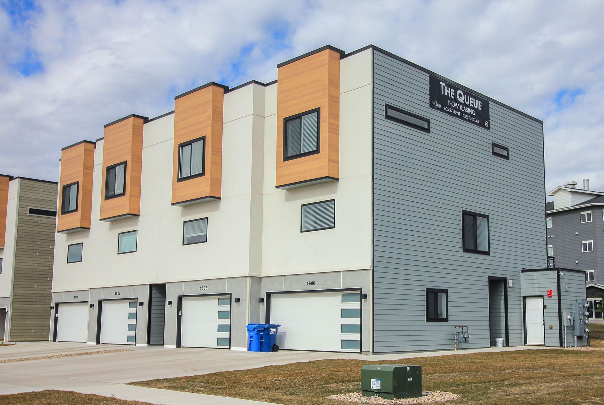 Modern townhouse-style apartment building with white, gray, and orange exterior panels and garage doors