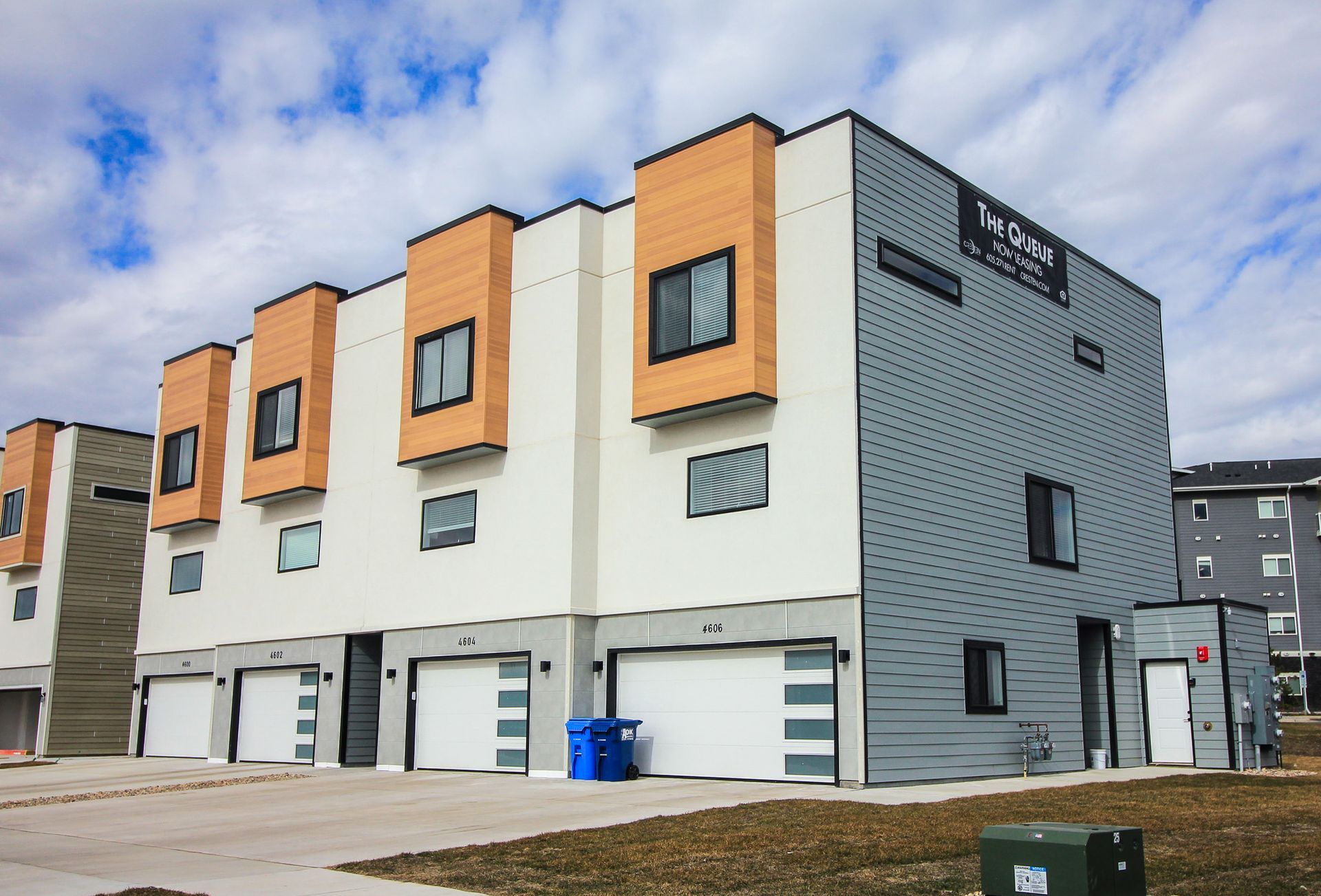 Modern townhouse row with orange and gray facades, garage doors, and a cloudy sky.