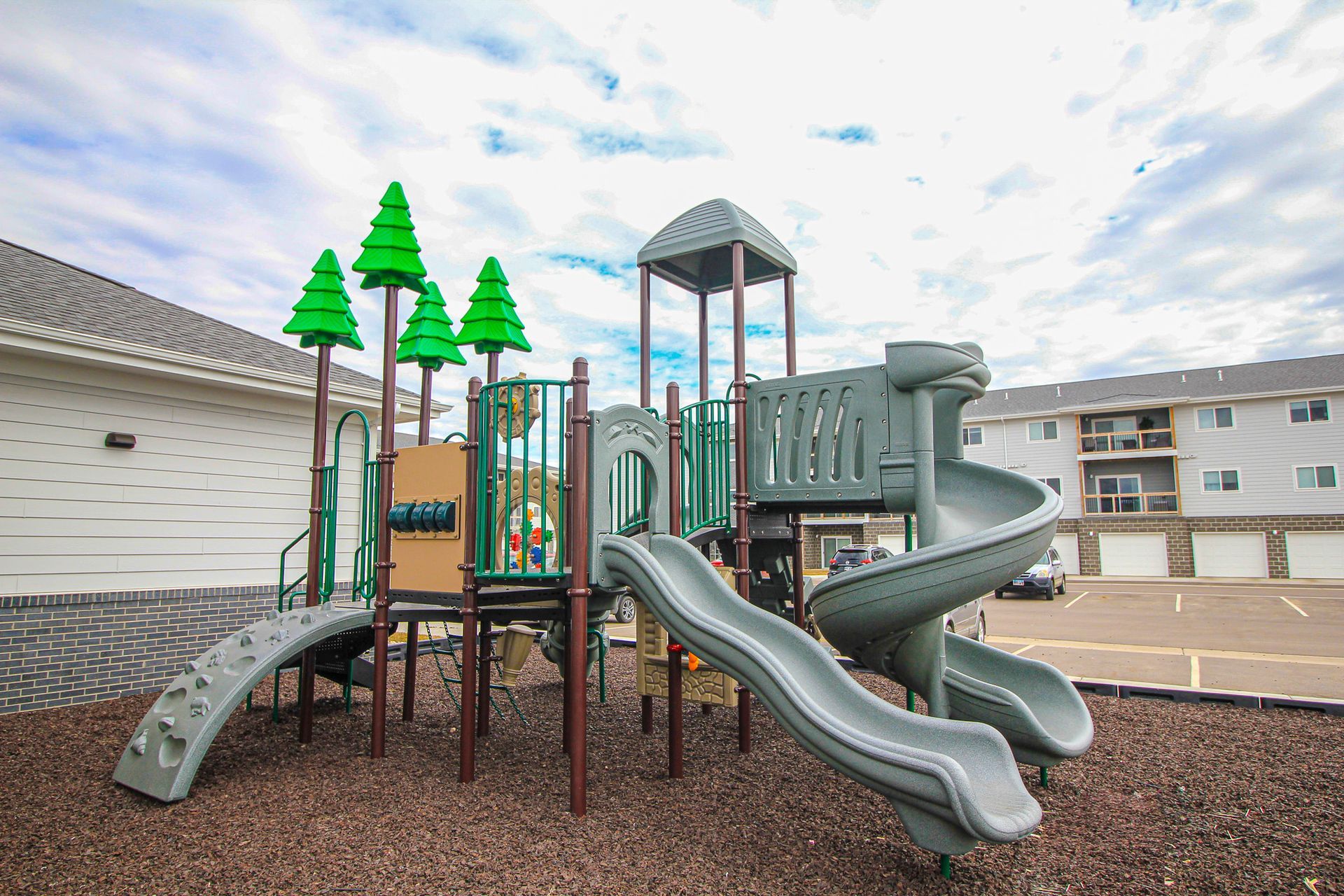 Outdoor playground with gray slides, green accents, and a climbing tower in a residential courtyard.