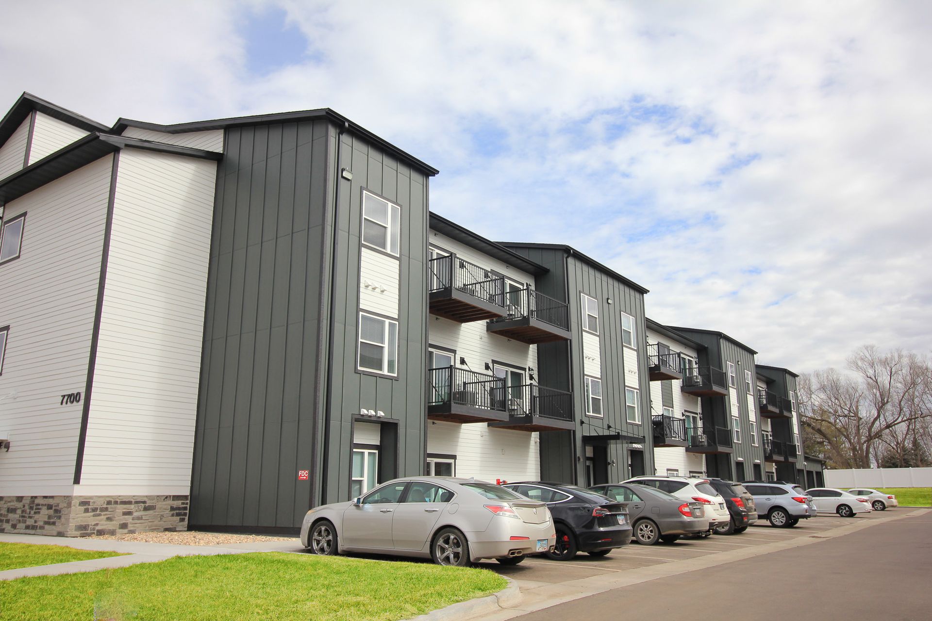 Apartment building exterior with parked cars along a street under a cloudy sky