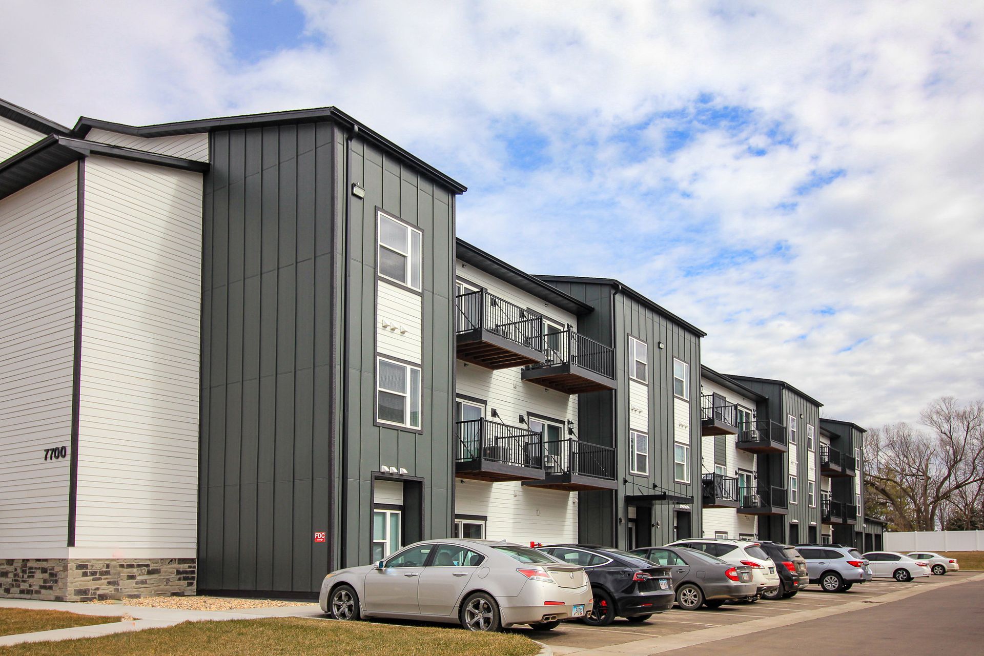 Modern apartment building with balconies and parked cars under a cloudy sky