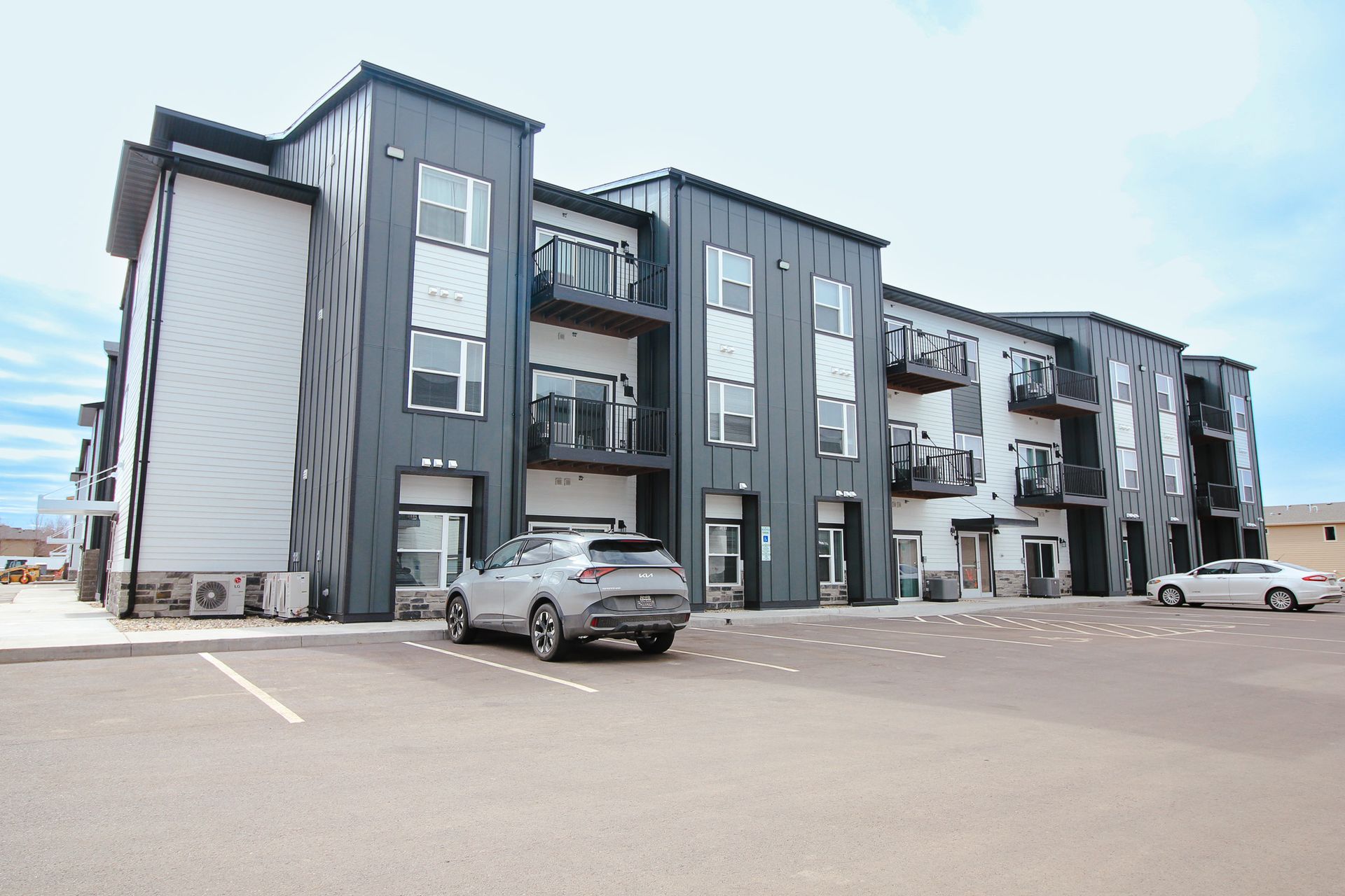Modern gray apartment building with balconies and parked cars in a lot