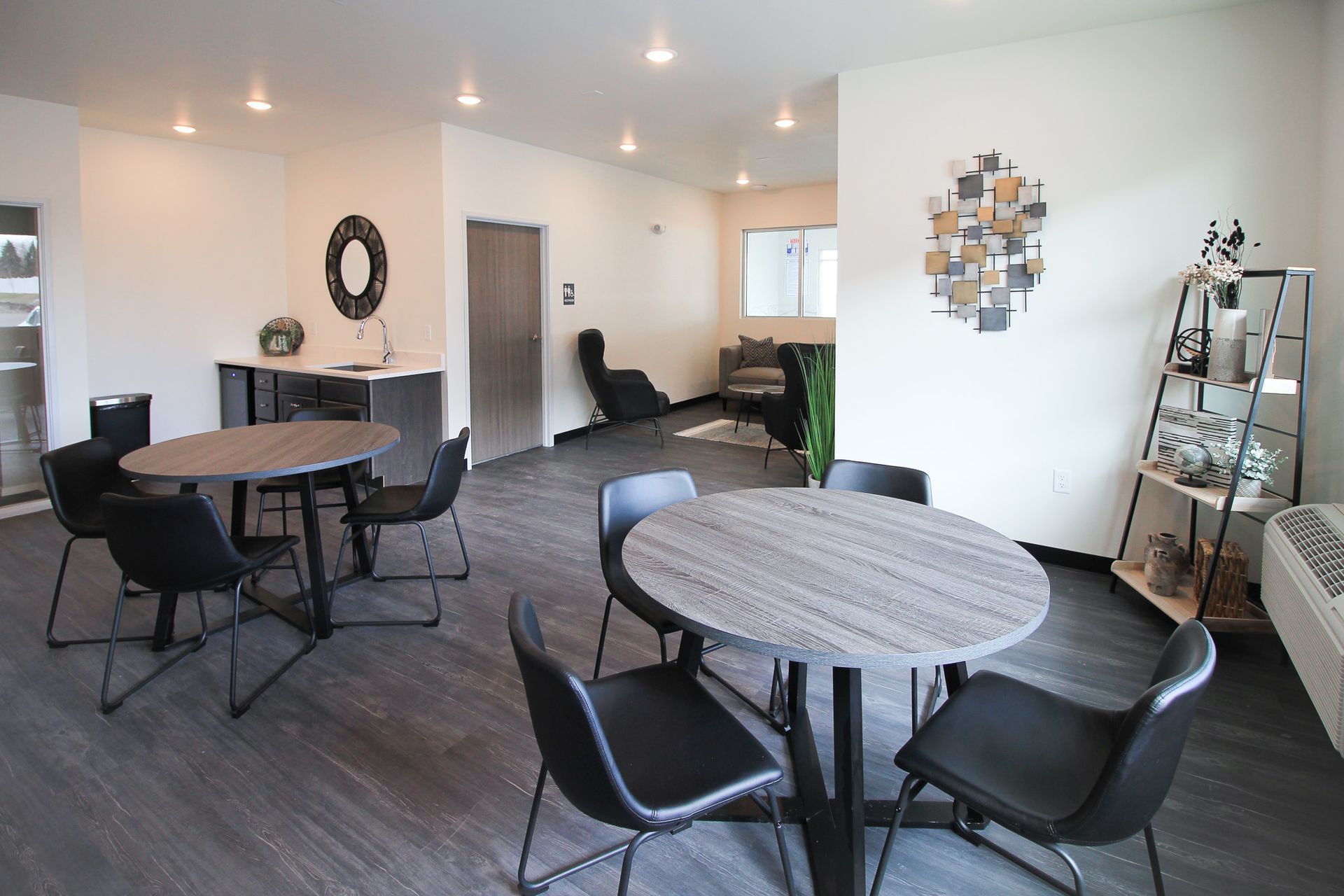 Modern open office lounge with round tables, black chairs, white walls, and pendant lights