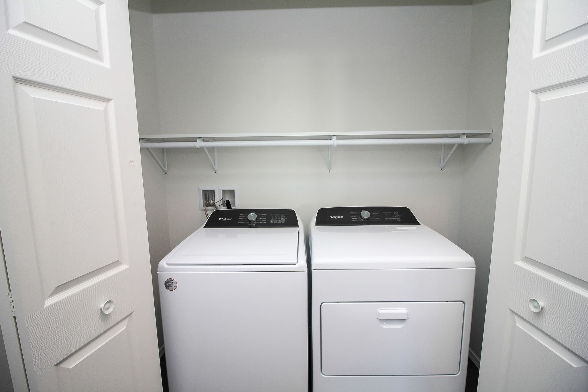 Laundry closet with a washer, dryer, and white shelving behind open doors
