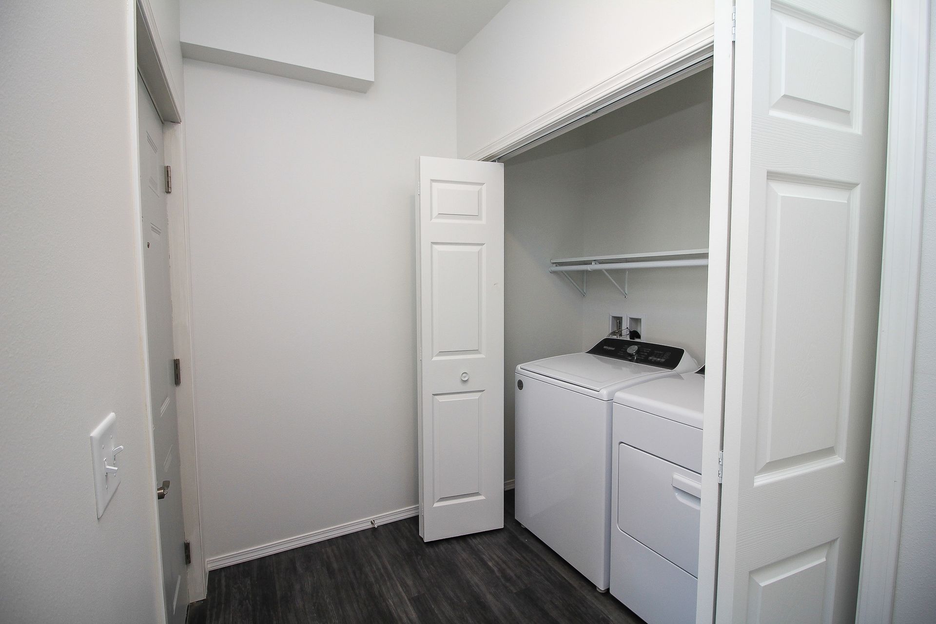 Empty laundry closet with white cabinets, shelf, and dark wood floor in a light gray room