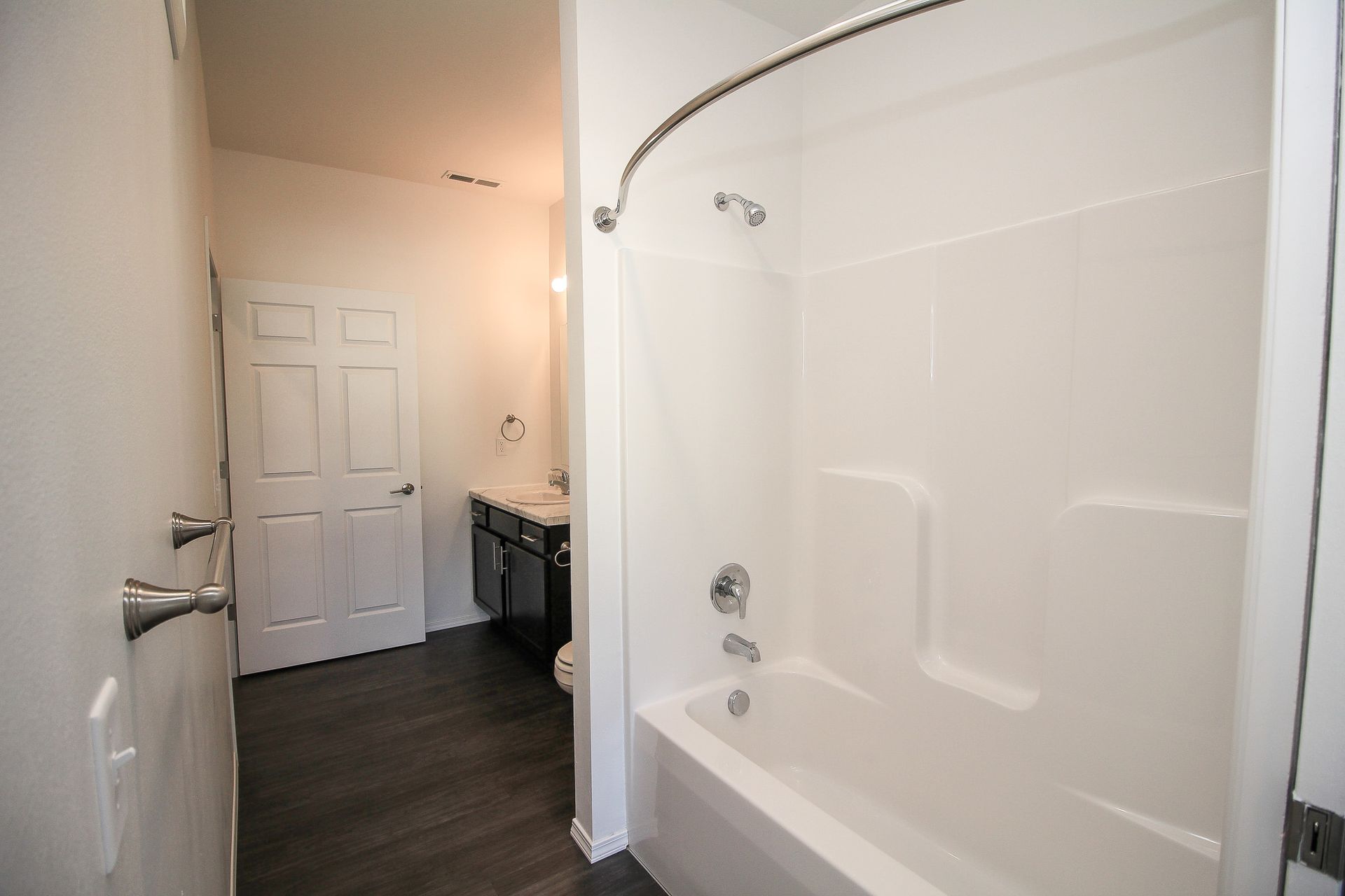 Bathroom with a white bathtub, shower rod, and beige walls leading to a hallway with a door.