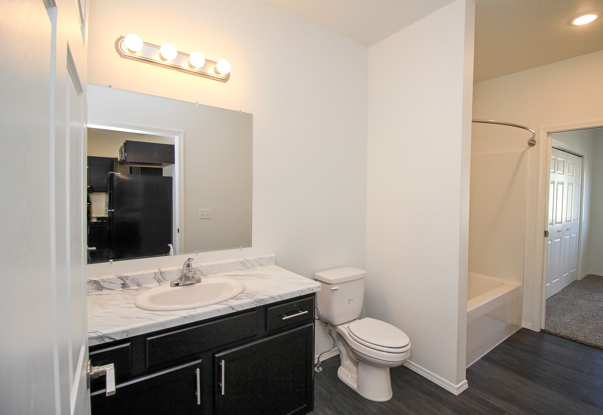 Bathroom with dark vanity, large mirror, toilet, and adjacent hallway with carpet and built-in shelving