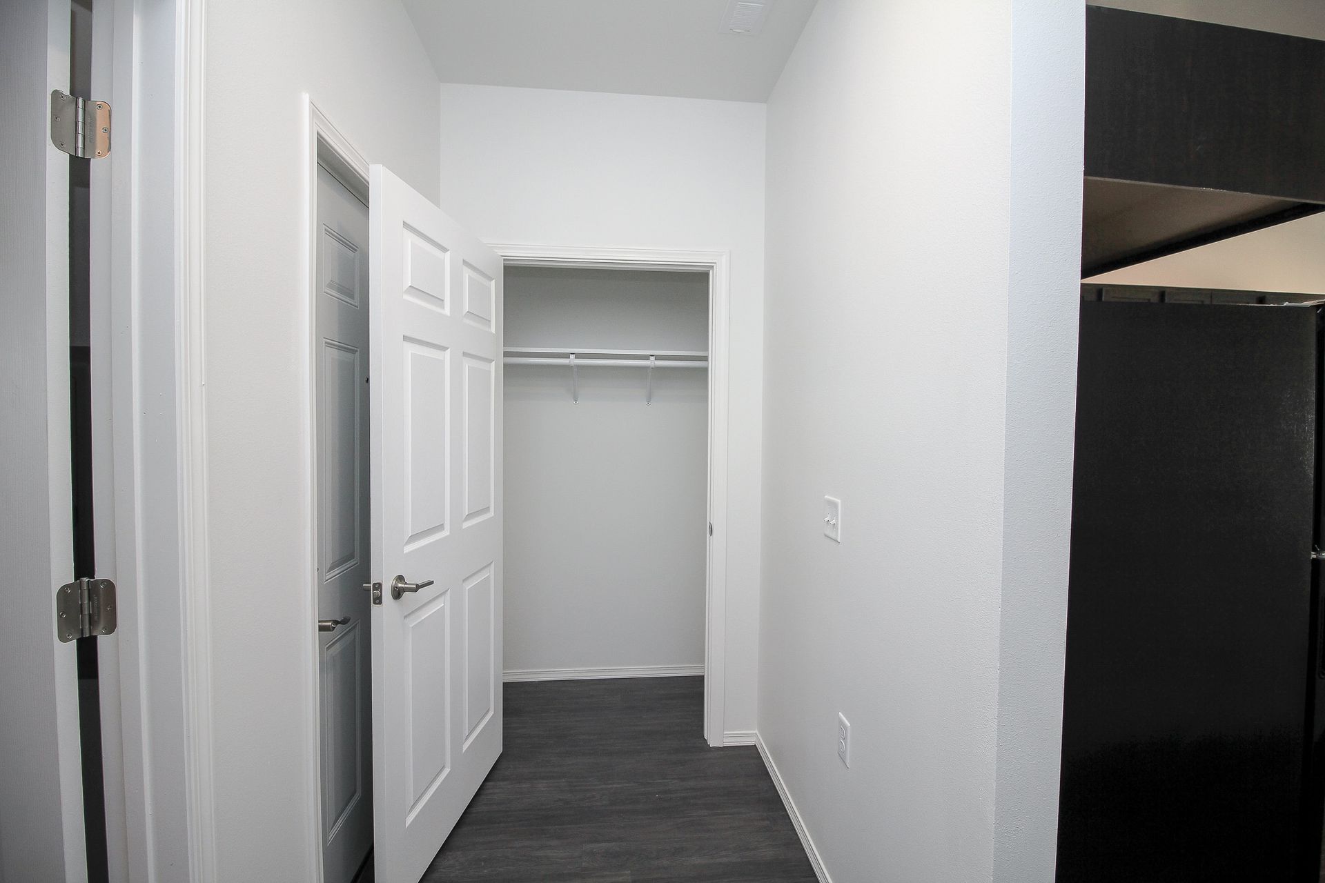 Narrow white hallway with an open closet and a partially visible black cabinet