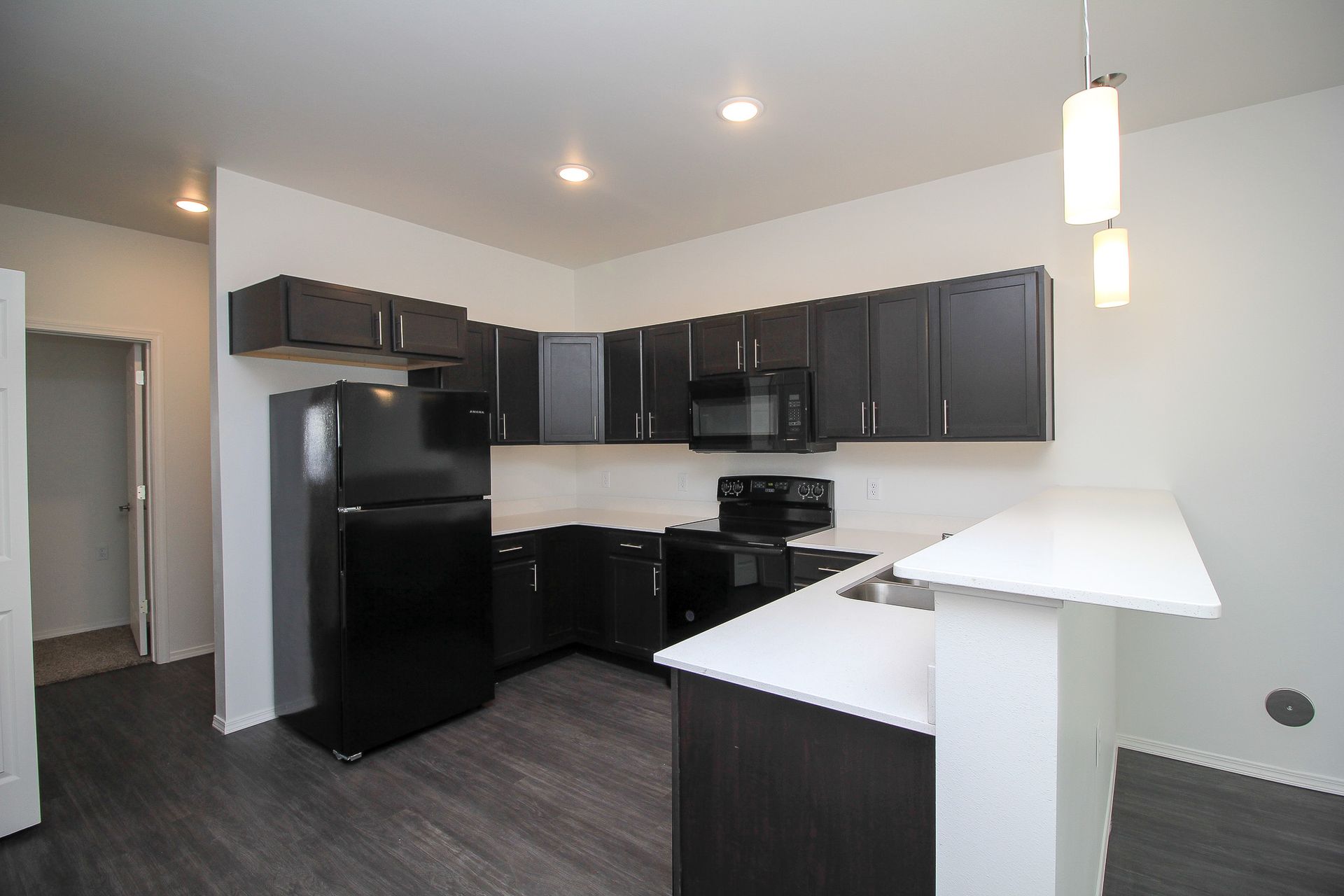 Modern kitchen with black appliances, dark cabinets, white countertops, and a breakfast bar