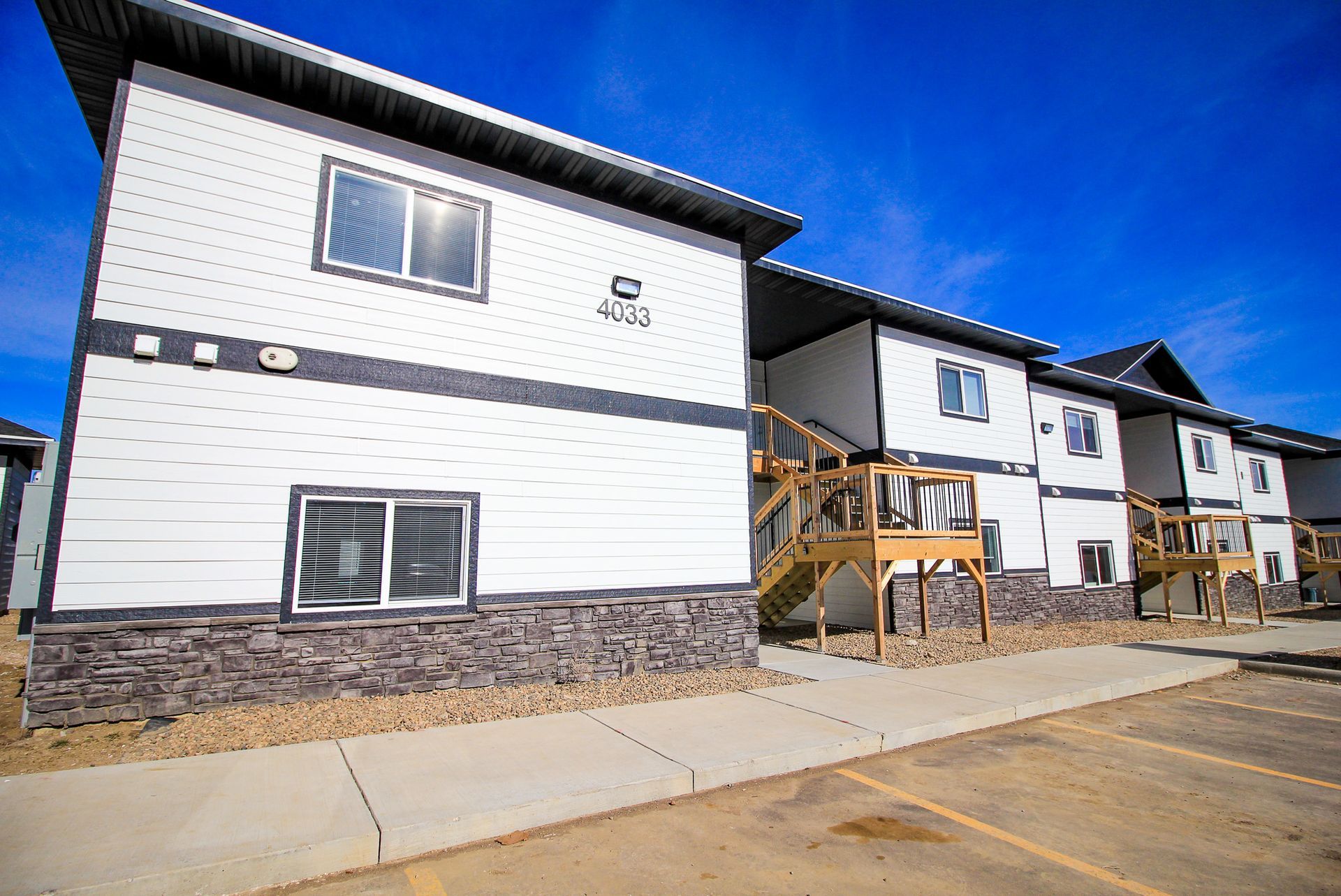 Row of modern white townhouses with dark roofs and wooden balconies along a paved street