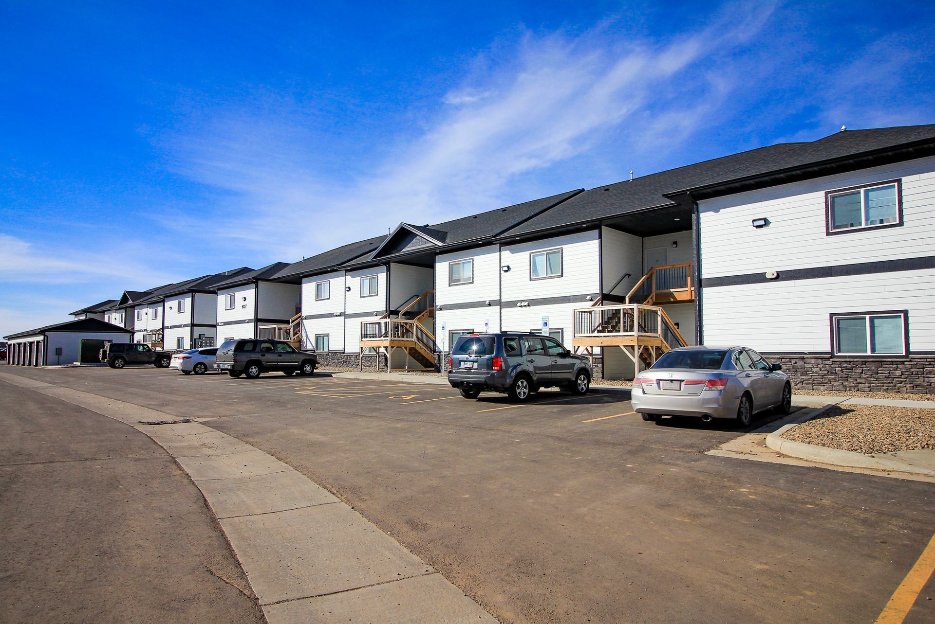 Row of modern white townhouses with parked cars along a paved street under a blue sky