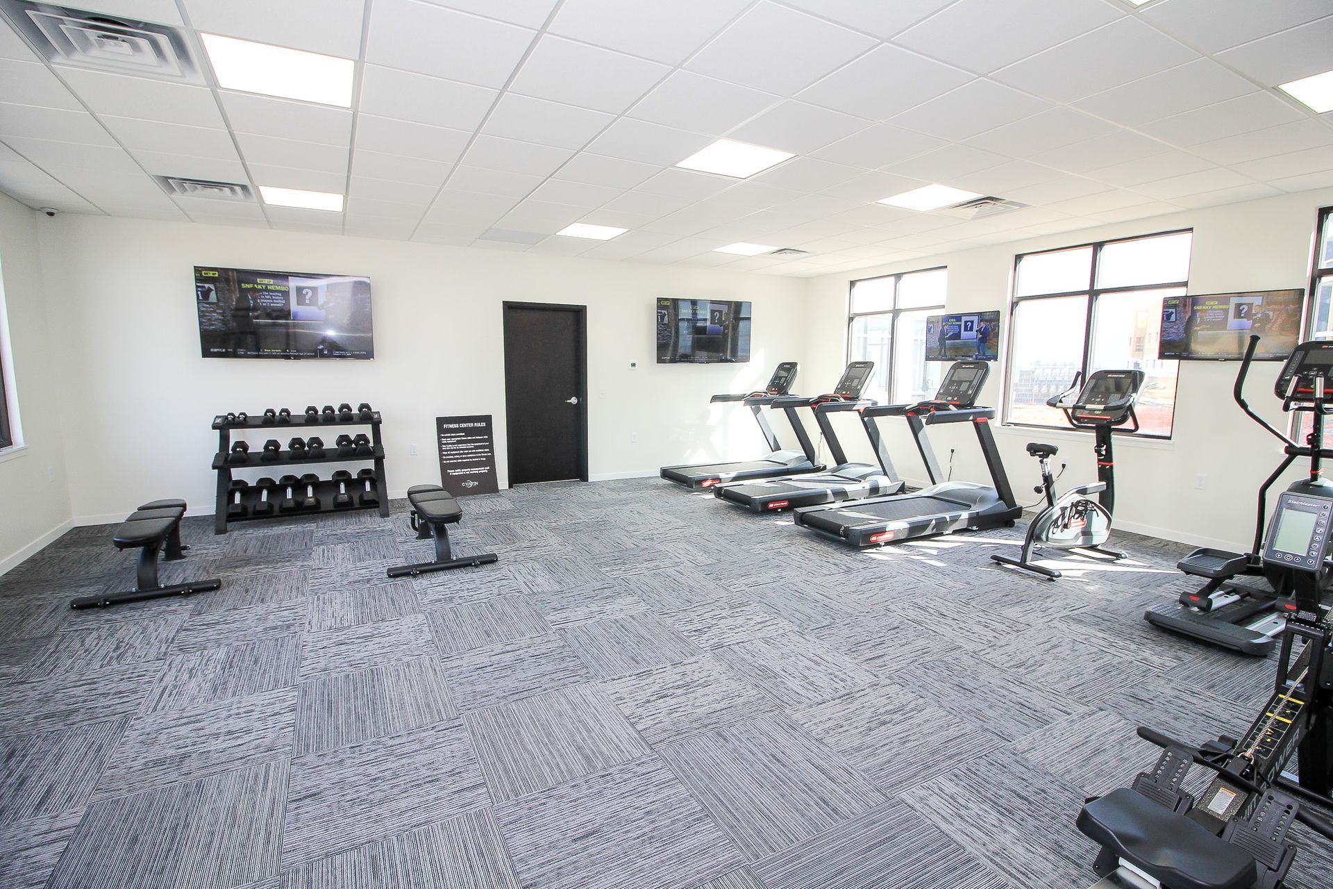 Modern gym room with treadmills, weights, benches, and large windows