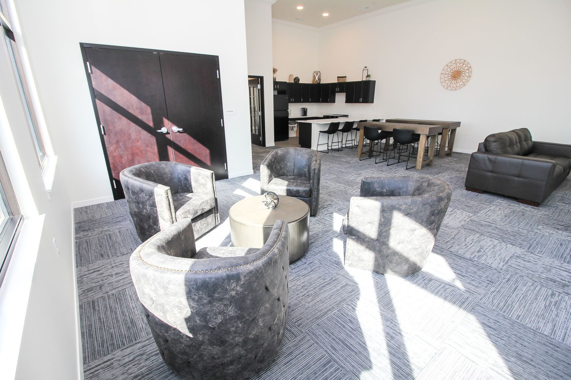 Modern living room with gray chairs, sofa, coffee table, and bright sunlight on carpet