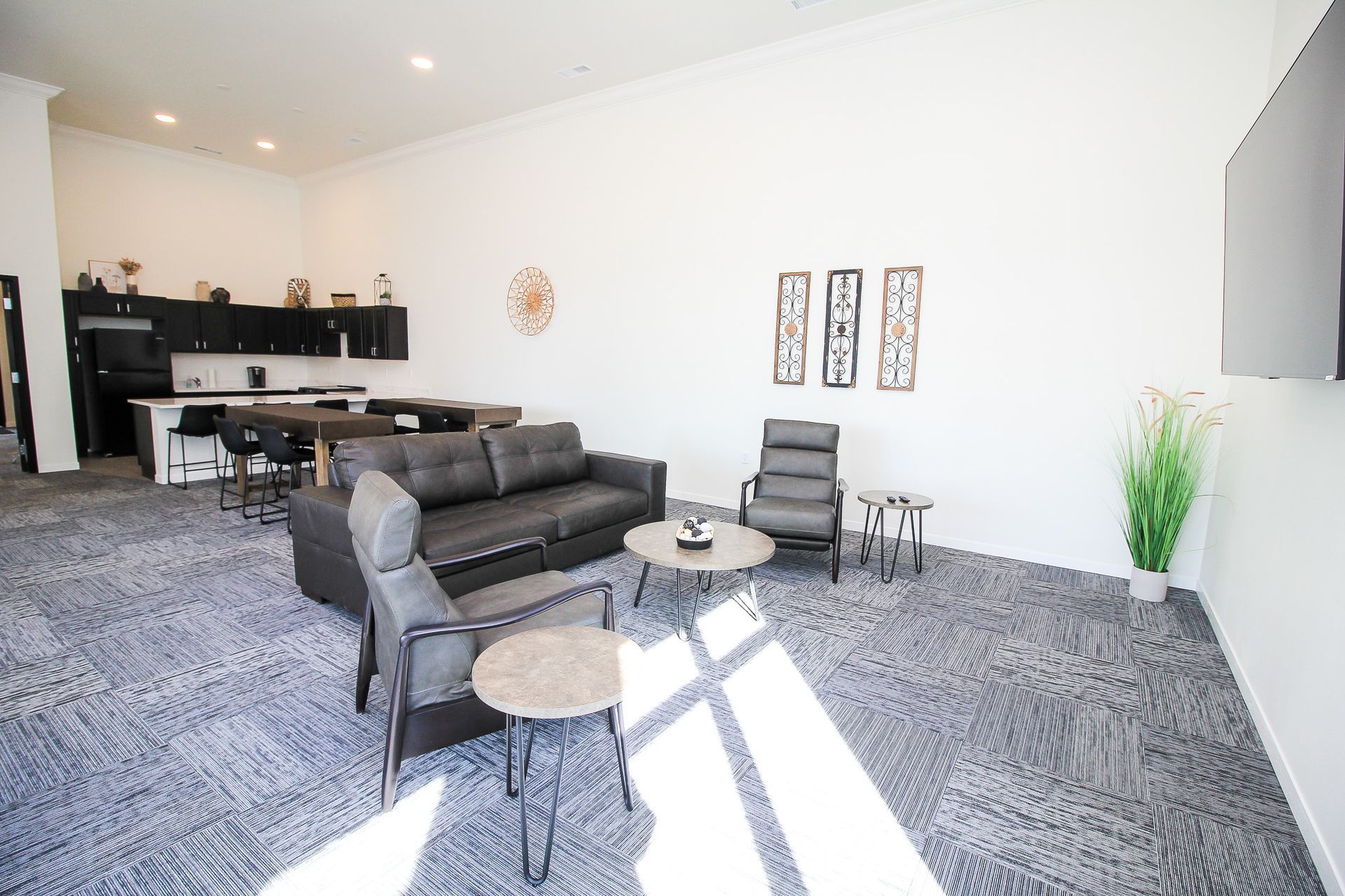 Spacious modern living room with gray sectional sofa, chairs, small tables, and wall decor on a carpeted floor