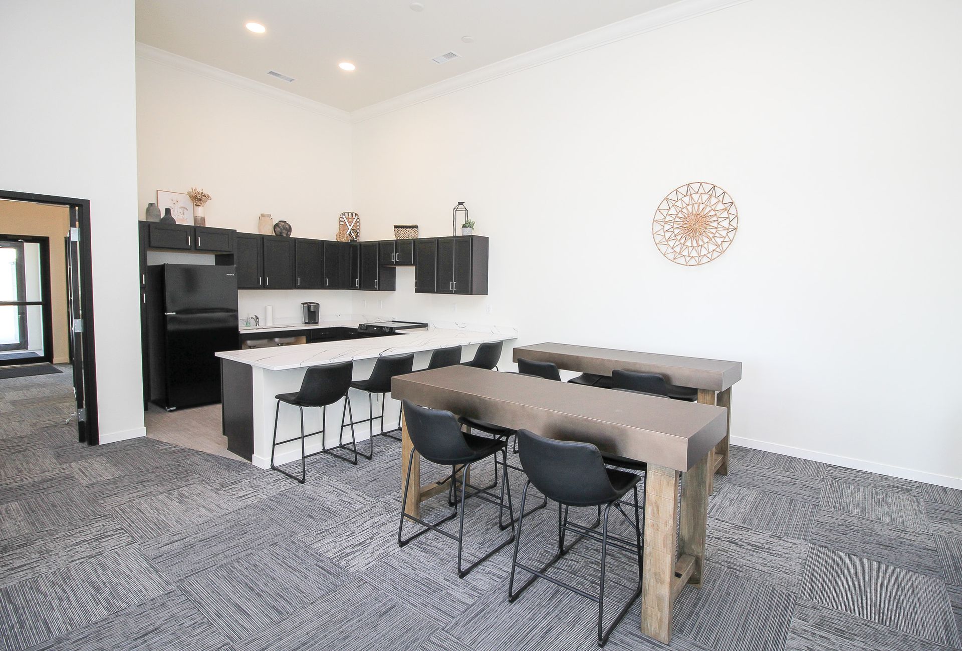 Modern open-plan kitchen and dining area with black cabinets, gray carpet, and a wooden table with chairs