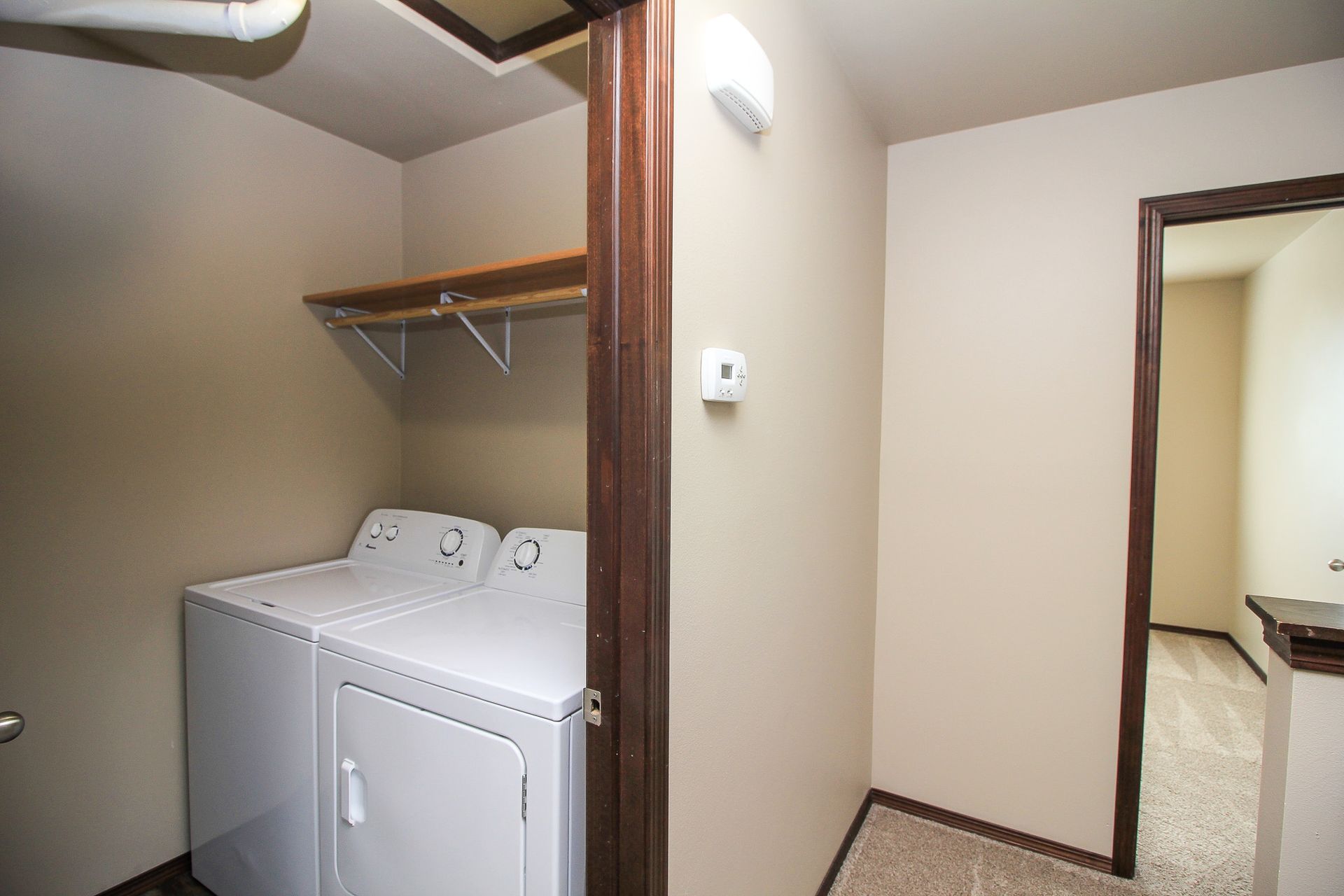 Laundry closet with a dryer, open shelf, and doorway into a beige hallway