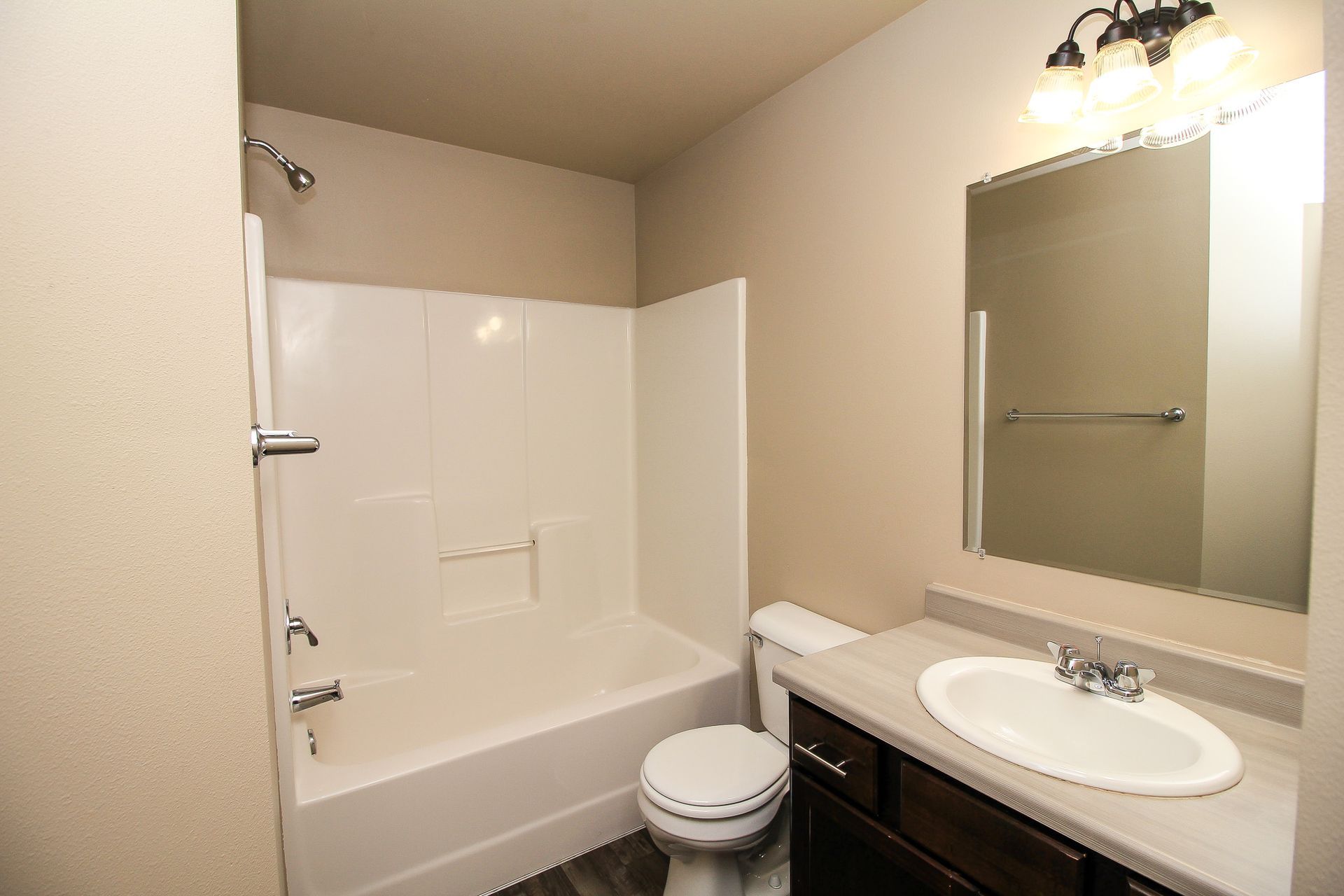 Small beige bathroom with tub, toilet, sink vanity, and mirror under wall lights.