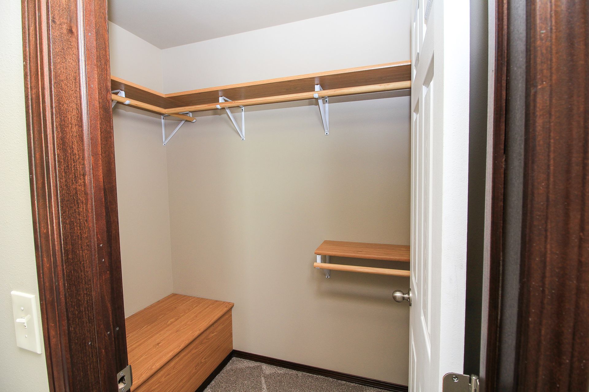 Empty walk-in closet with beige walls, white shelving, and wood trim.
