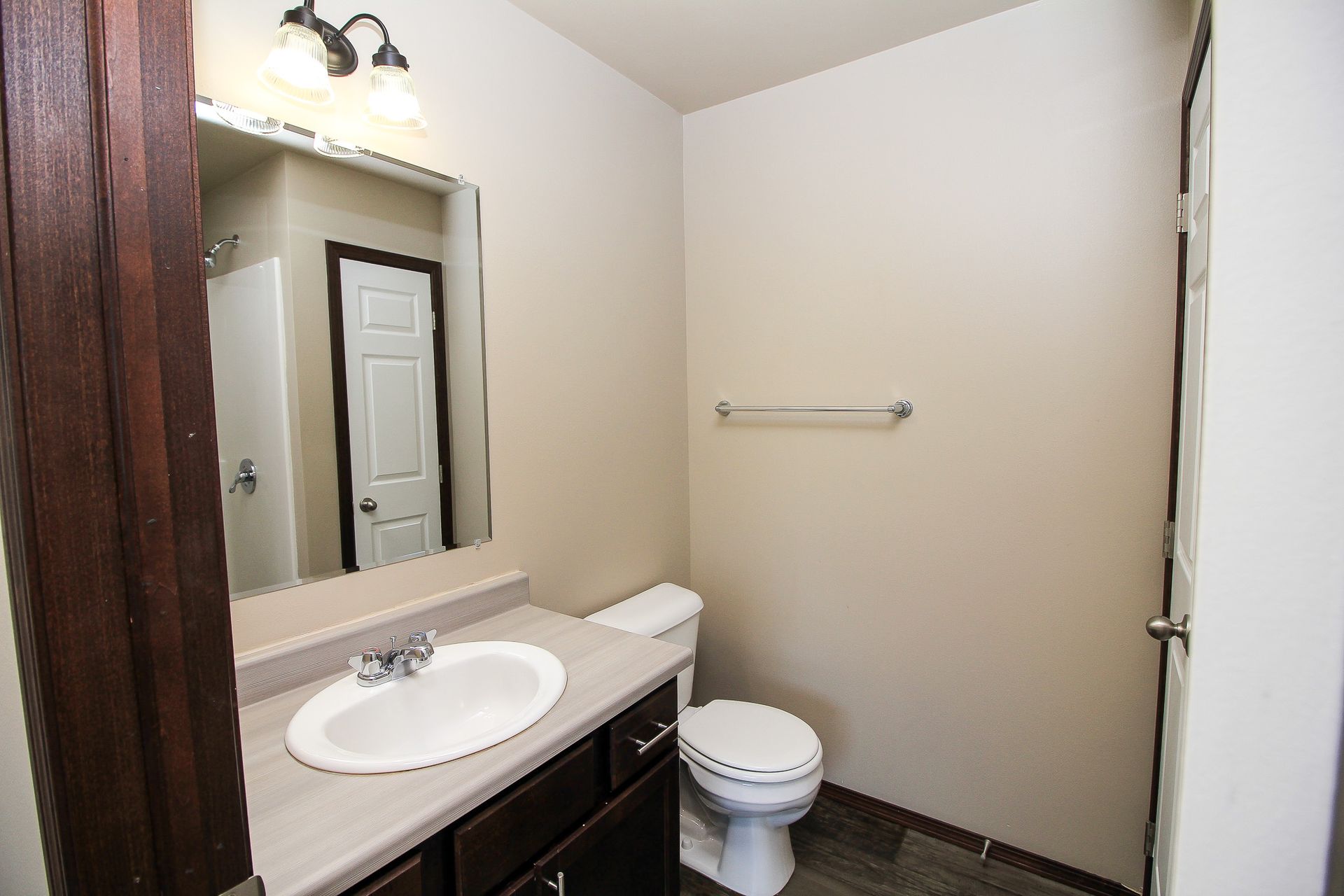 Small bathroom with vanity sink, mirror, toilet, towel bar, and beige walls.