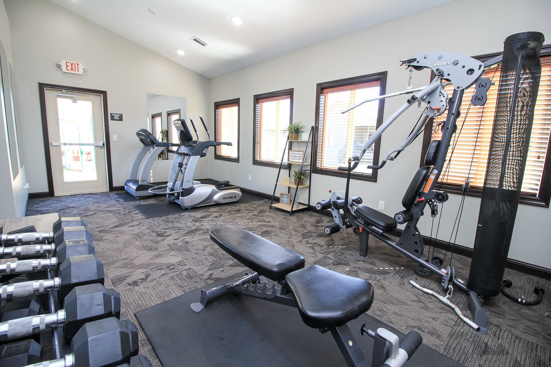 Small home gym with exercise bikes, weight bench, cable machine, and large windows