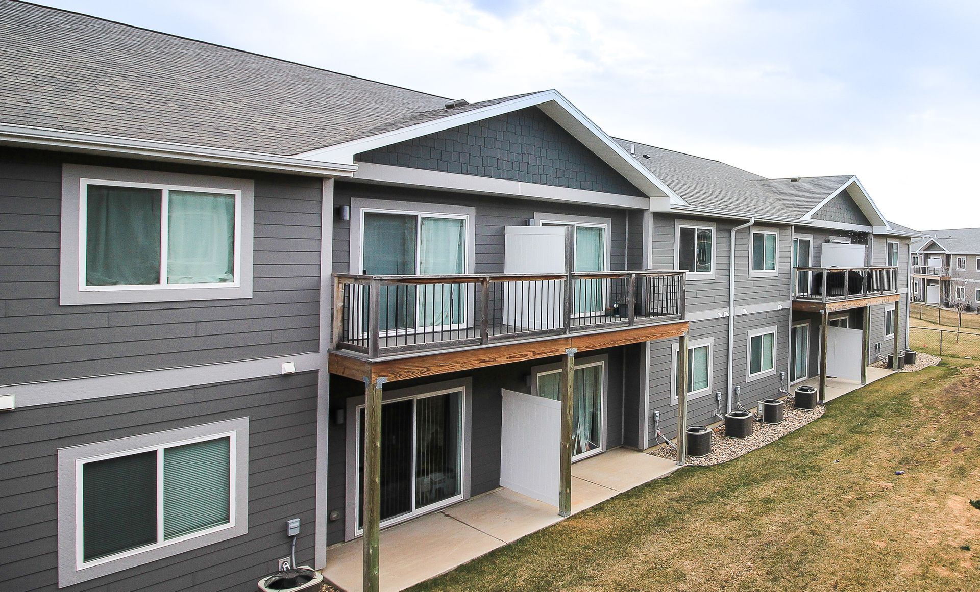 Modern gray apartment building with balconies and sliding glass doors along a grassy slope