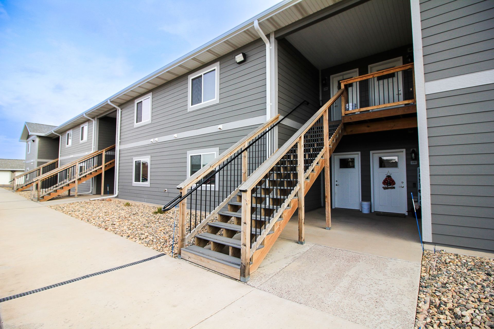 Apartment building exterior with gray siding, front staircases, and covered walkways