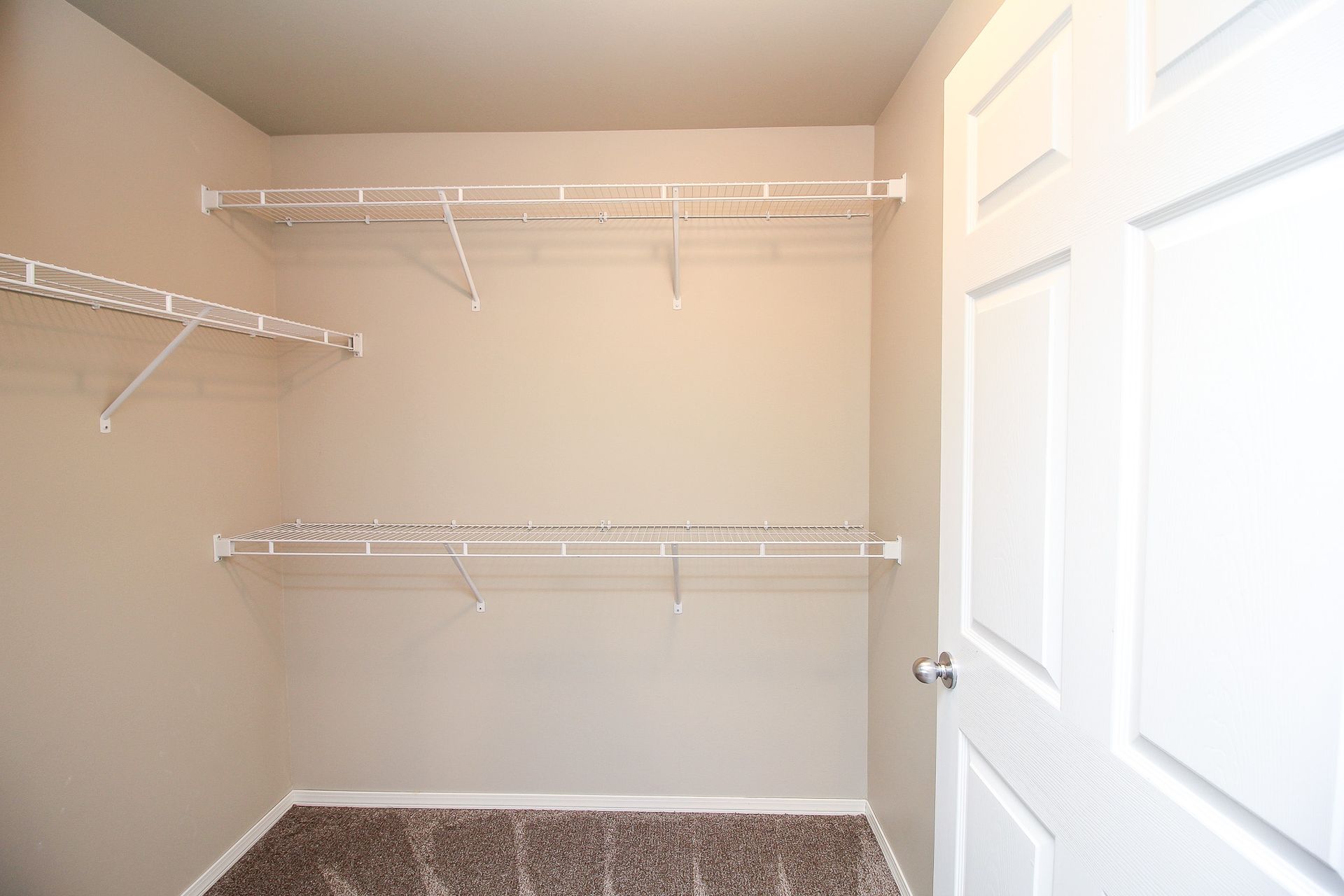 Empty walk-in closet with white wire shelving and a white door.