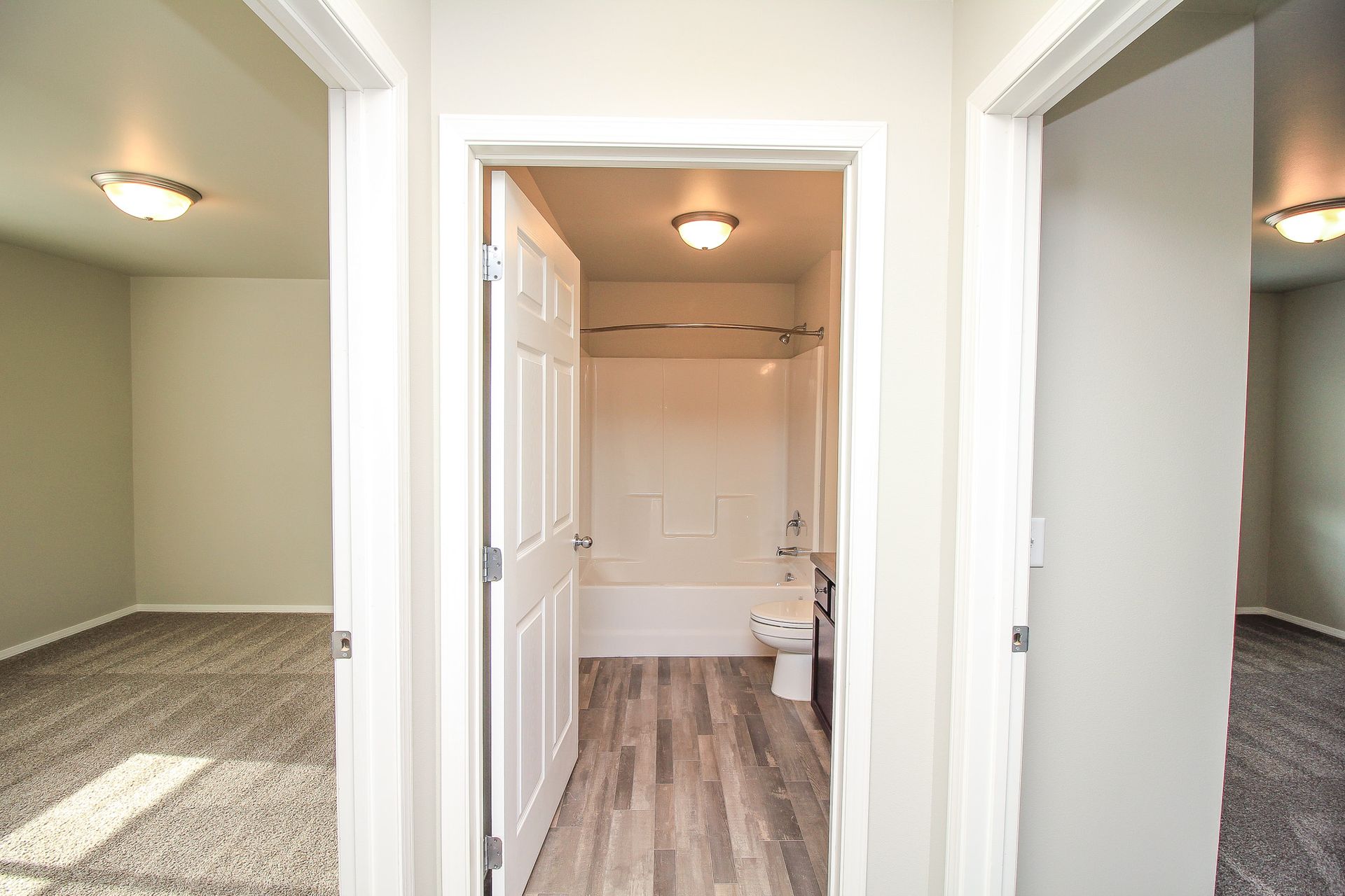 Empty hallway with open doors to two carpeted rooms and a small closet with wood flooring.
