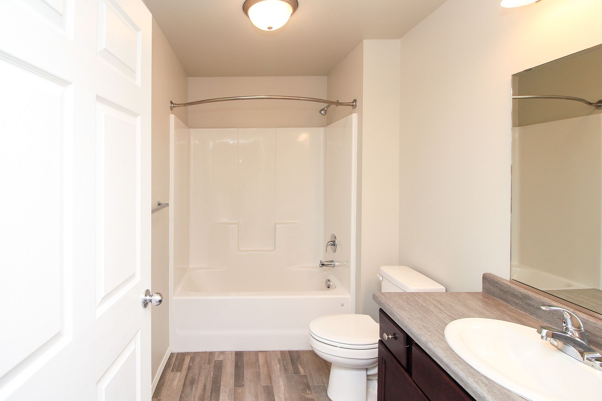 Bright bathroom with bathtub, toilet, vanity sink, and wood-look flooring