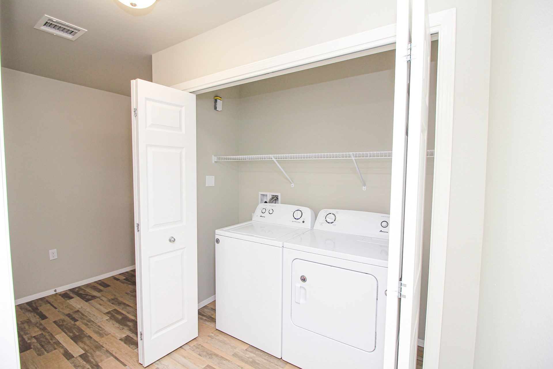 Laundry closet with white washer and dryer in a bright room with an open door
