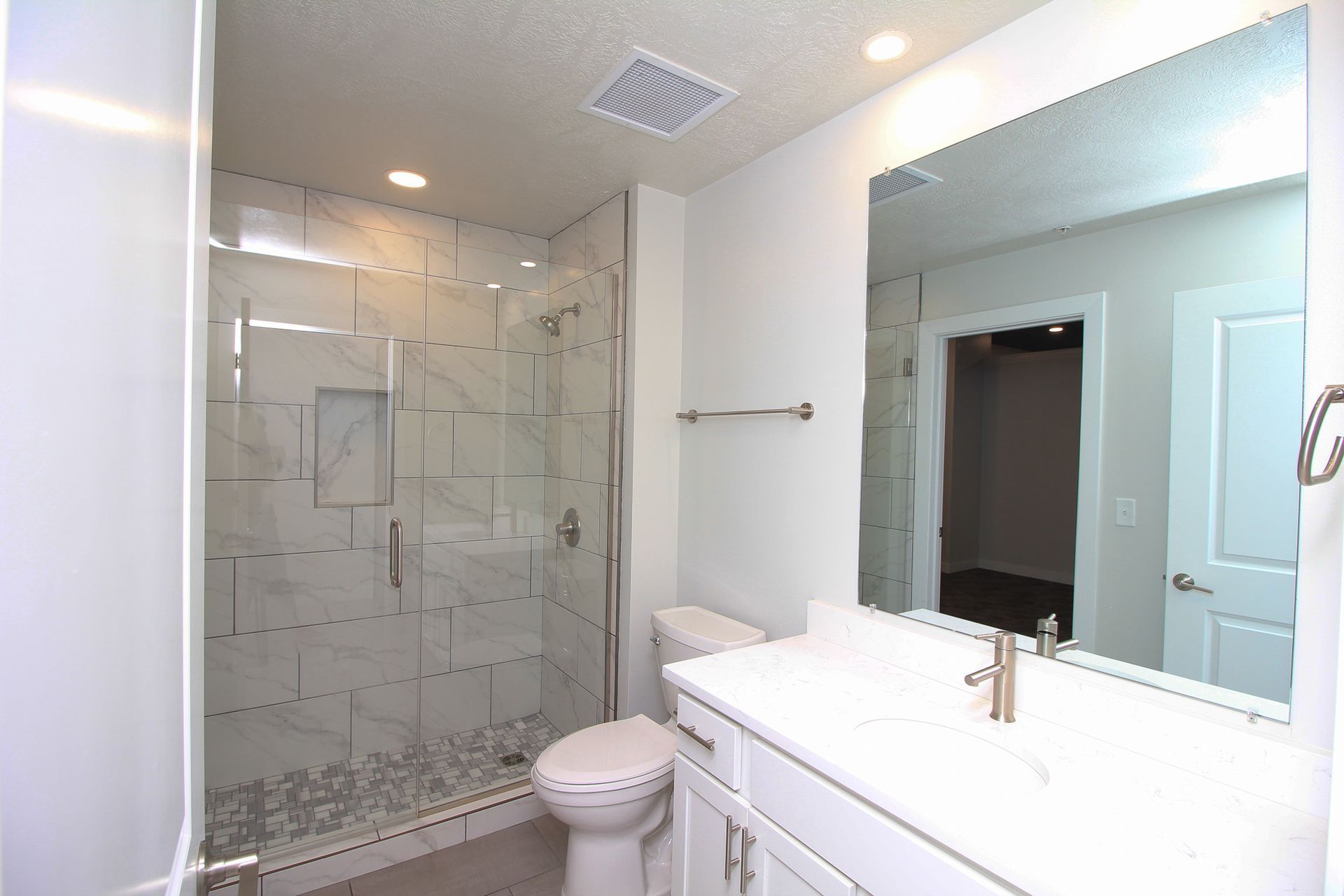 Bright modern bathroom with glass shower, white vanity, and large mirror