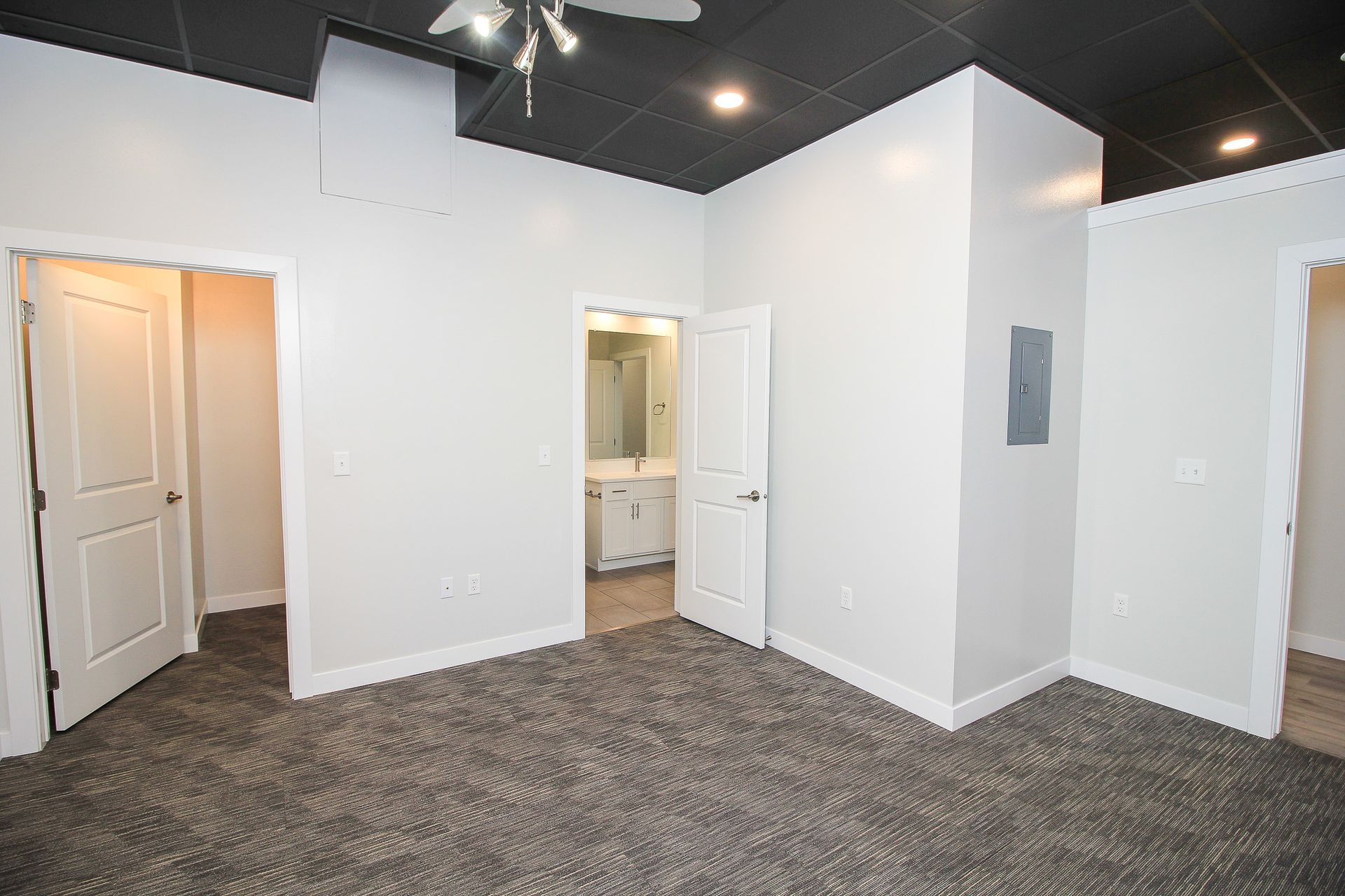 Empty carpeted room with white walls, open doors, and a small bathroom visible through the center doorway
