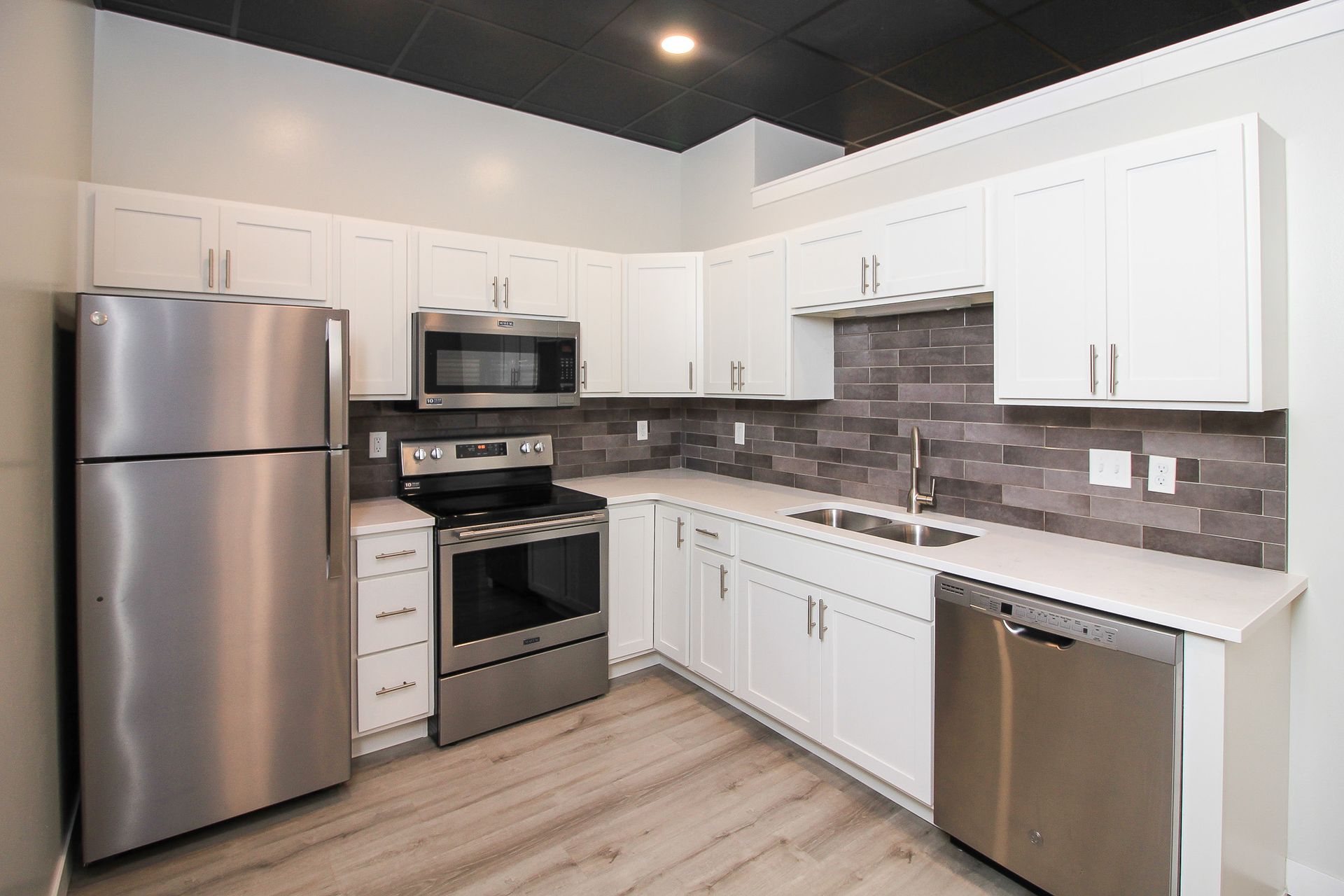 Modern white kitchen with stainless steel appliances, gray backsplash, and light wood flooring