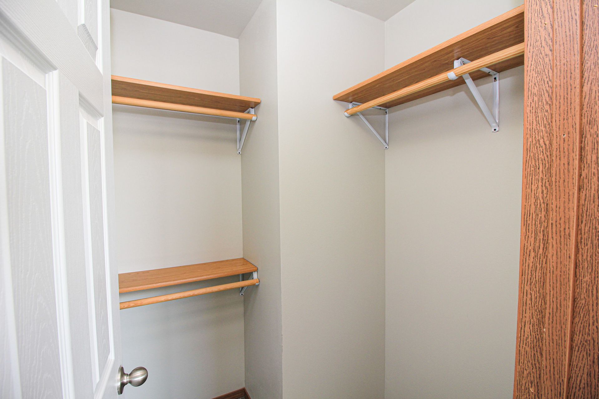 Empty walk-in closet with white walls, wood shelving, and a partially open door